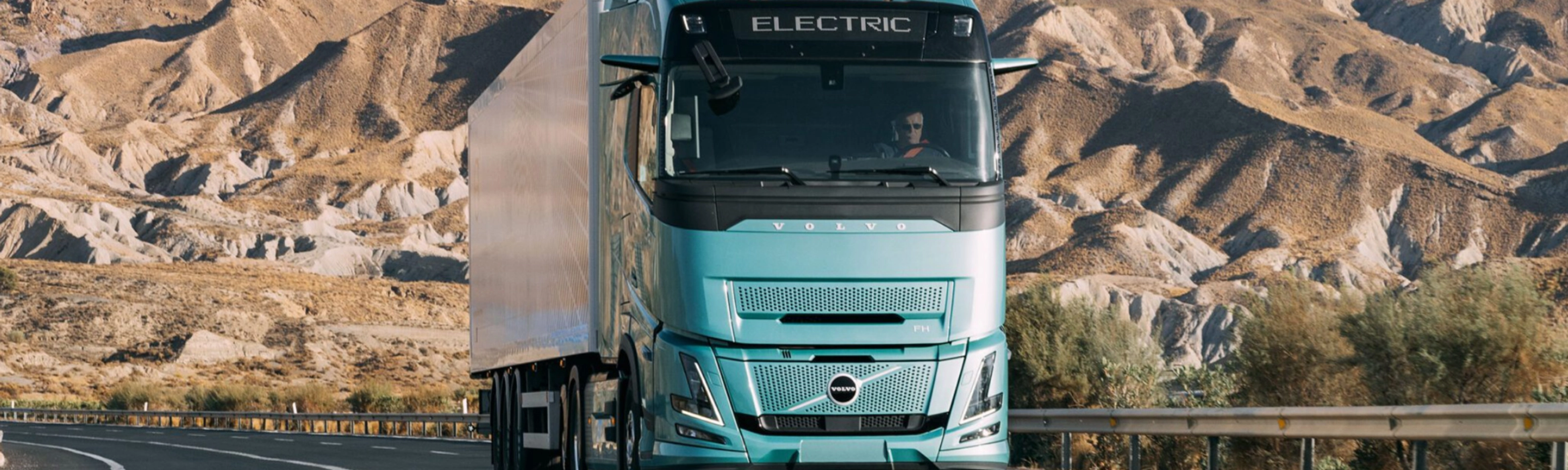 Volvo truck driving on a highway through a rocky desert landscape.