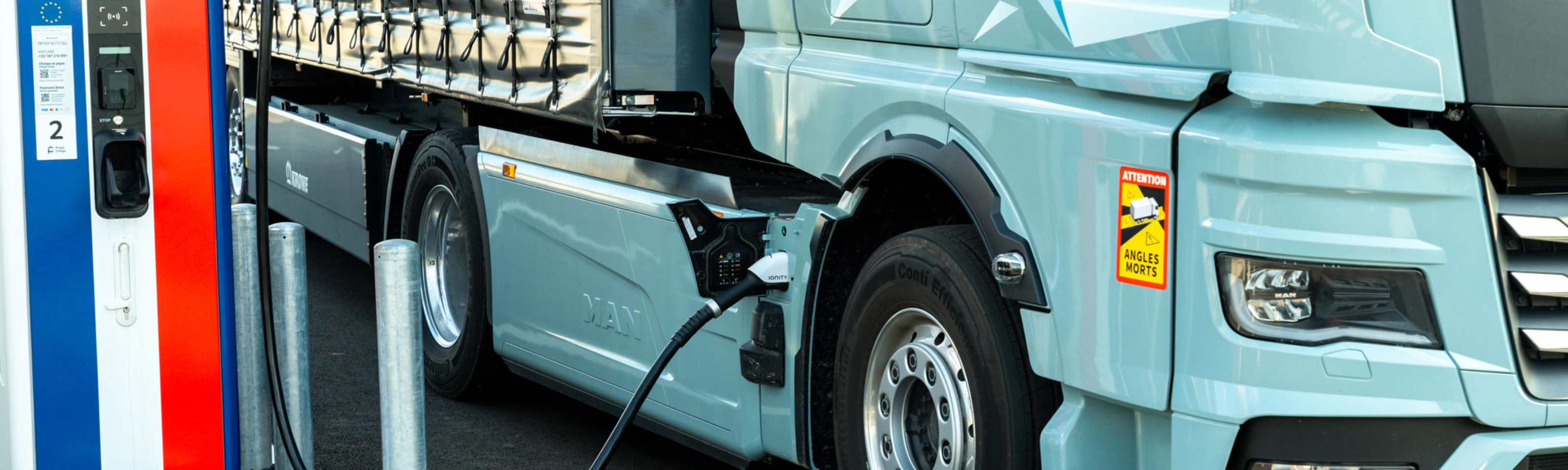 Electric truck charging at a public station, labeled 100% electric.