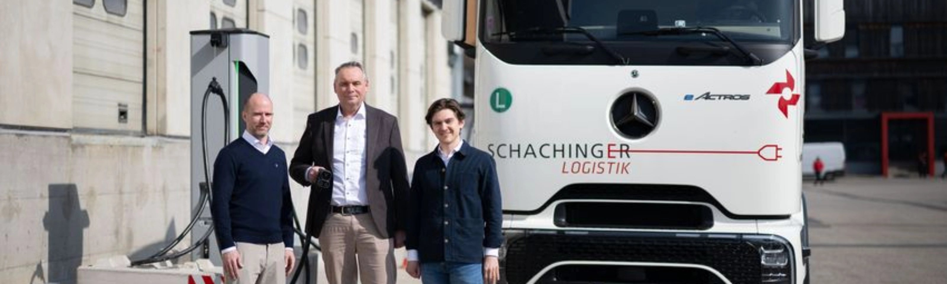 Three men standing in front of a white truck outside an industrial building.