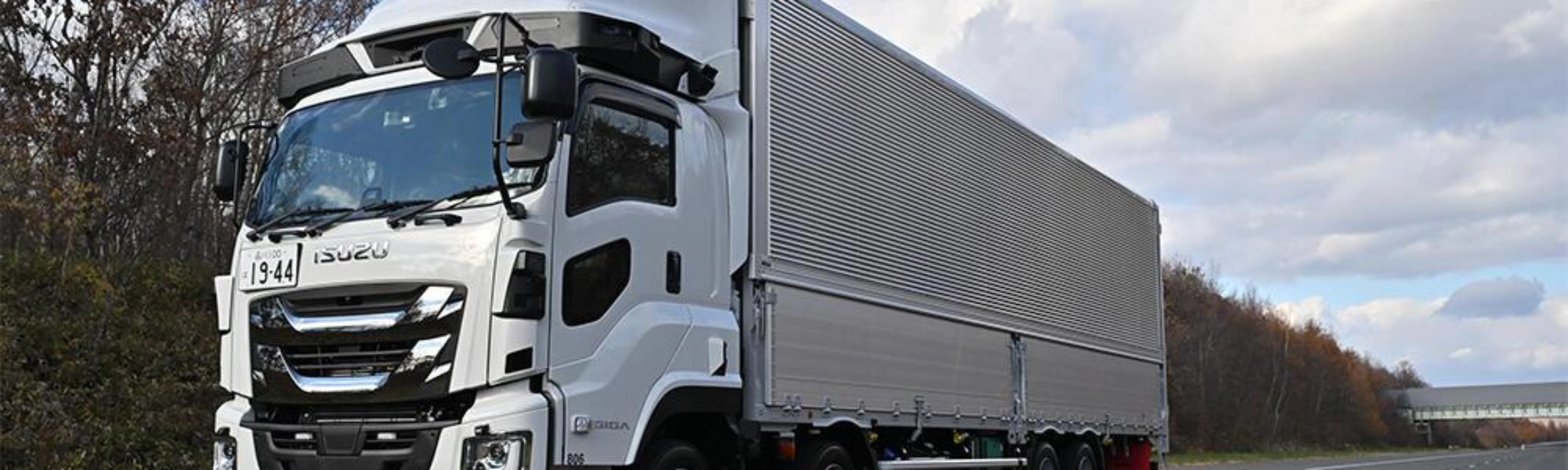 White semi-truck with trailer driving on a highway under a cloudy sky.