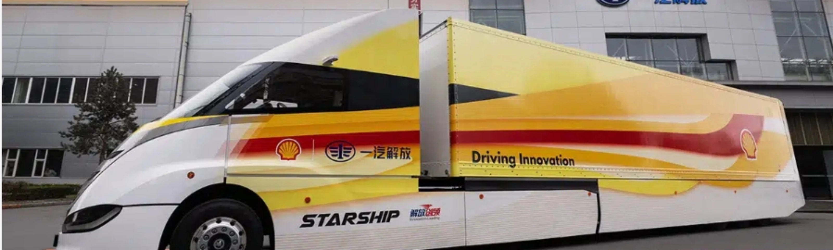 Weißer STARSHIP-Bus mit roten und gelben Streifen vor einem Industriegebäude bei Sonnenuntergang.