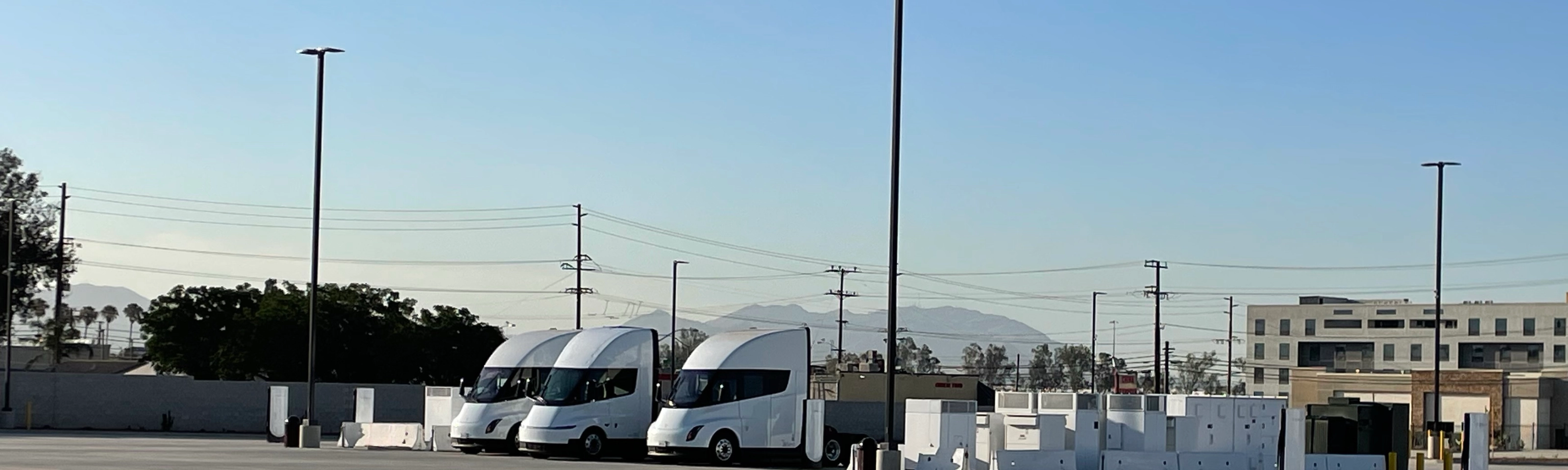 Three white electric trucks are parked at a charging station.