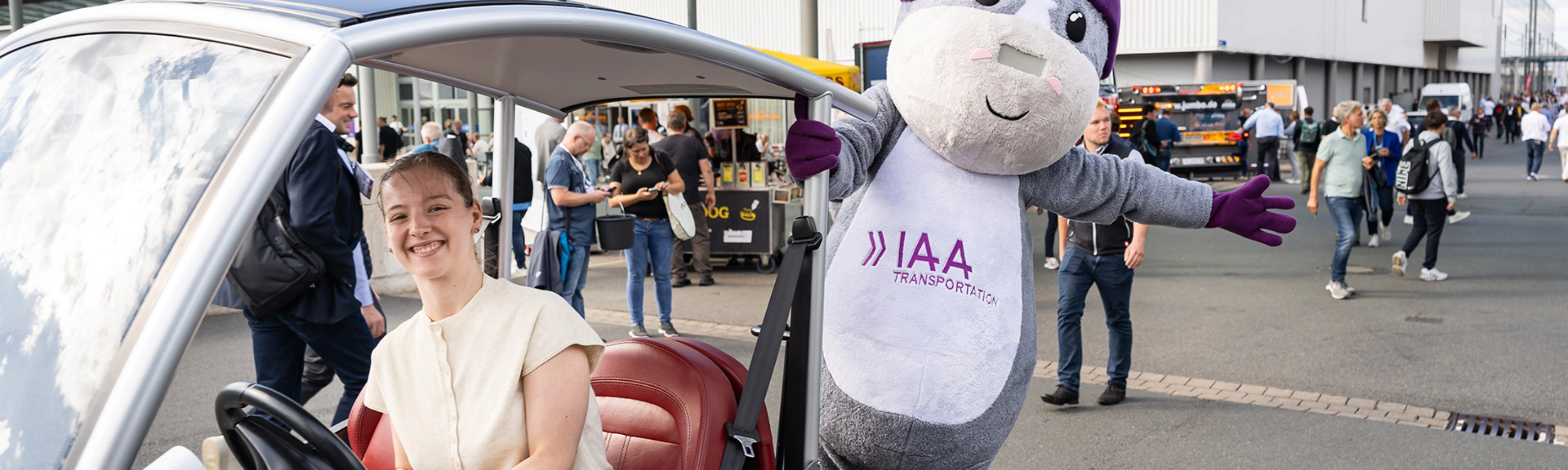 Frau in einem IAA-Fahrzeug neben dem IAA Transportation Maskottchen auf der Messe.