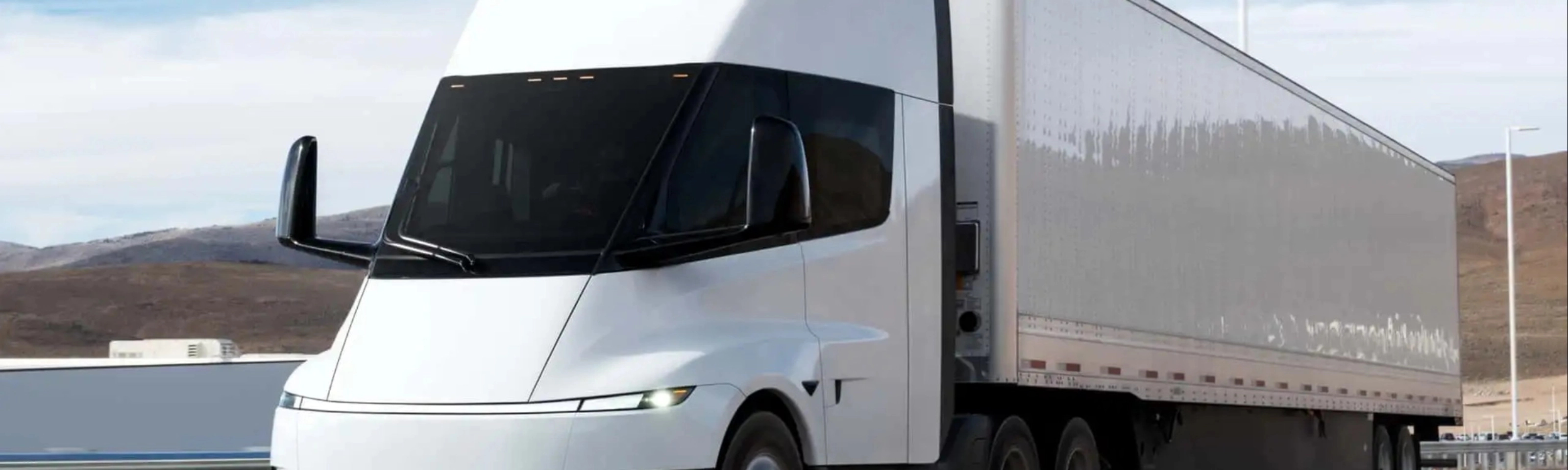 Electric semi-truck driving on a highway in a rural landscape.