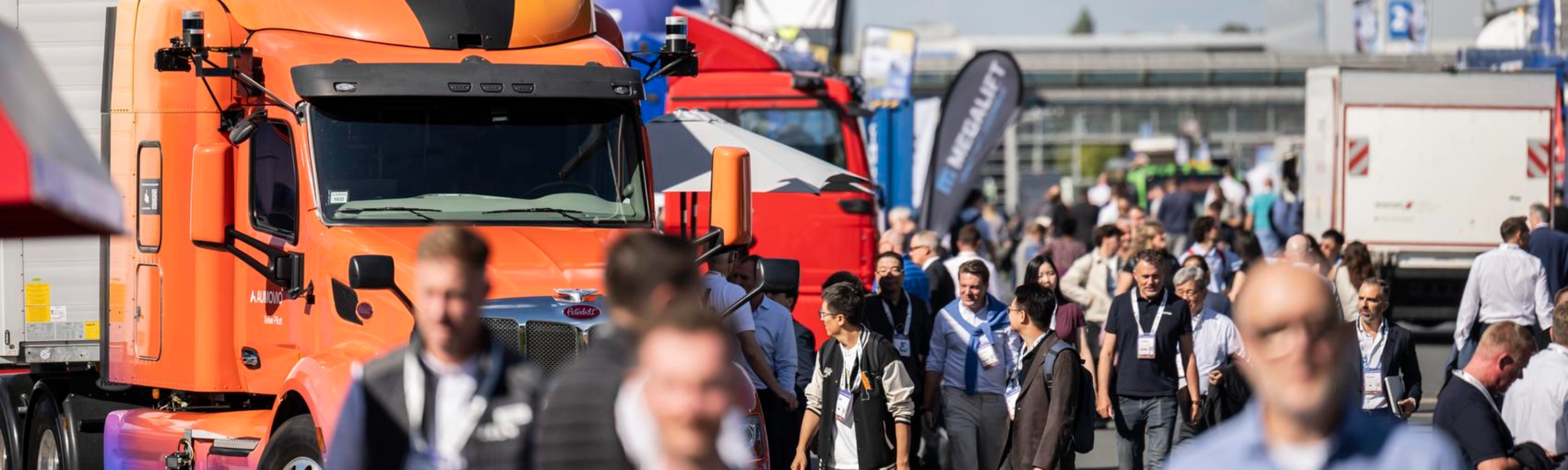 Besucher gehen auf einem belebten Messegelände zwischen Lkw hindurch.
