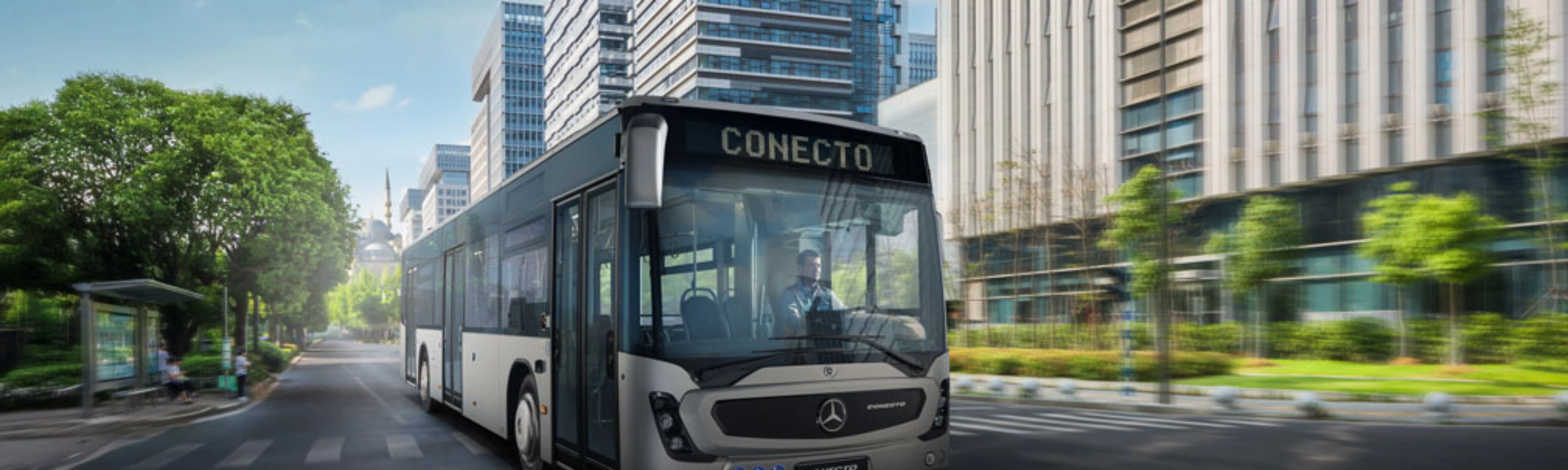 Modern city bus driving on a wide street between tall office buildings.