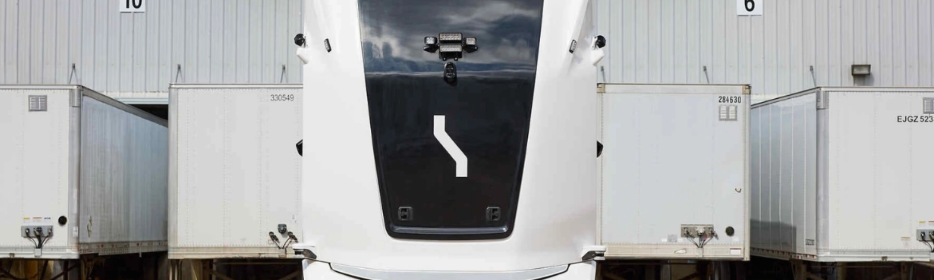 Einride autonomous electric truck in front of a warehouse with trailers.