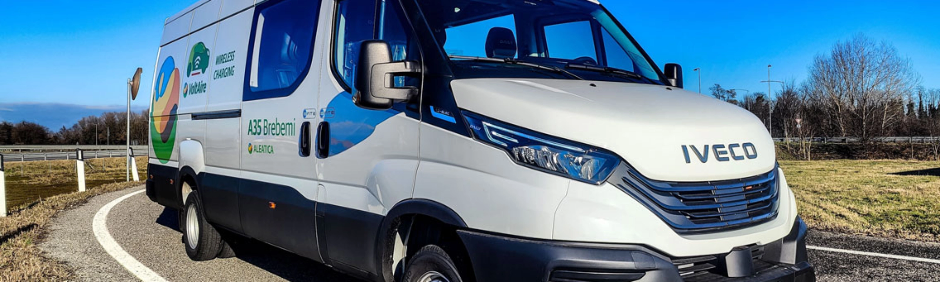 Ein weißer Iveco-Transporter fährt auf einer kurvigen Straße bei blauem Himmel.