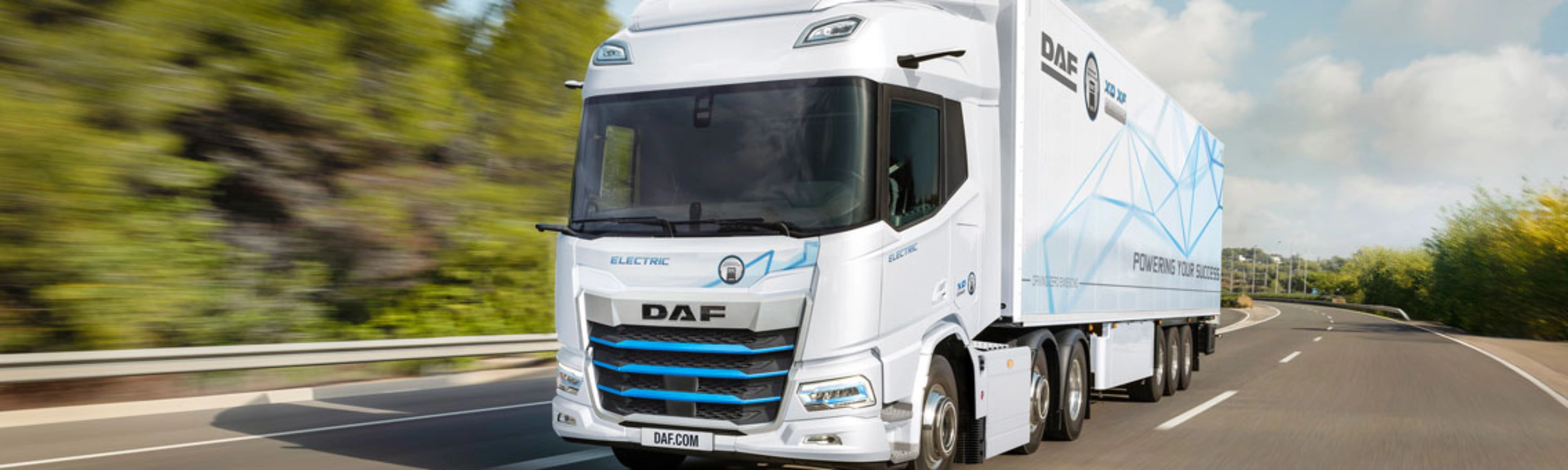 A white DAF electric truck is driving on a curved highway surrounded by greenery.