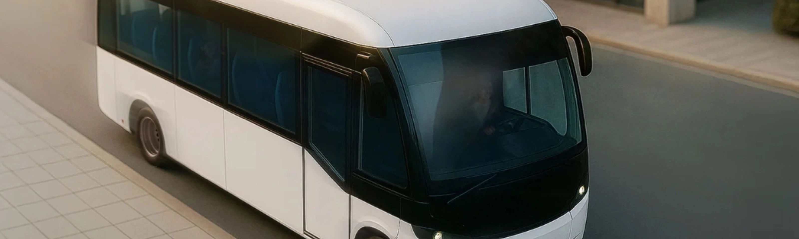 Small white autonomous shuttle bus driving on a city street, viewed from above.