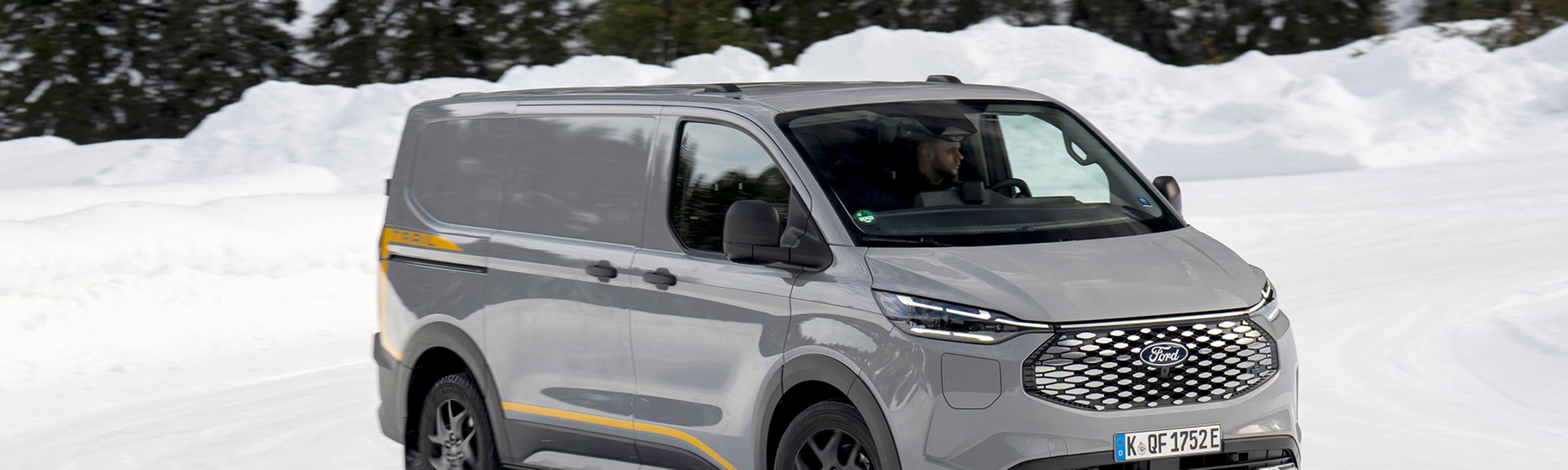 Grey Ford electric van driving on a snowy road with forest in the background.