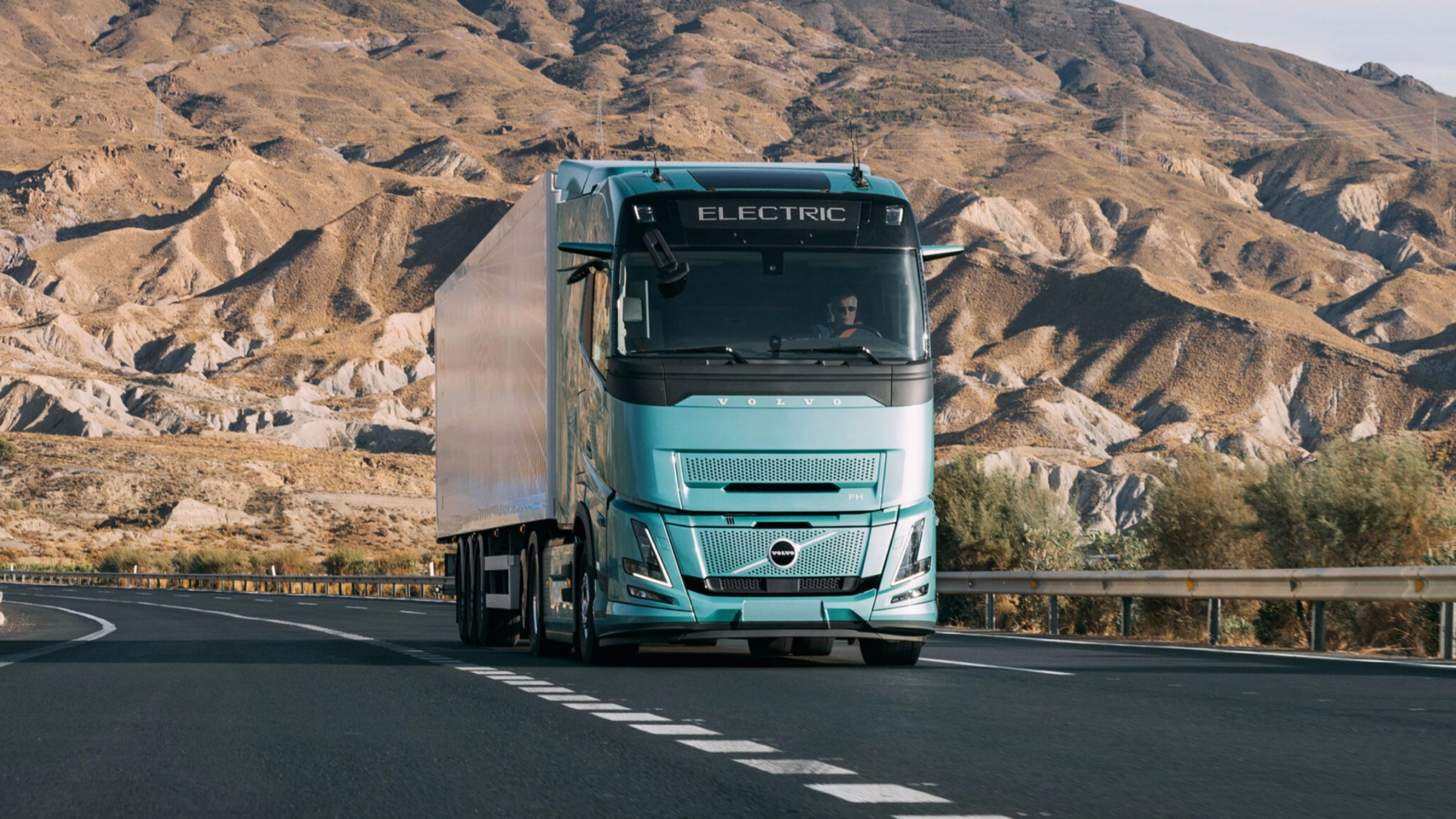 Volvo truck driving on a highway through a rocky desert landscape.