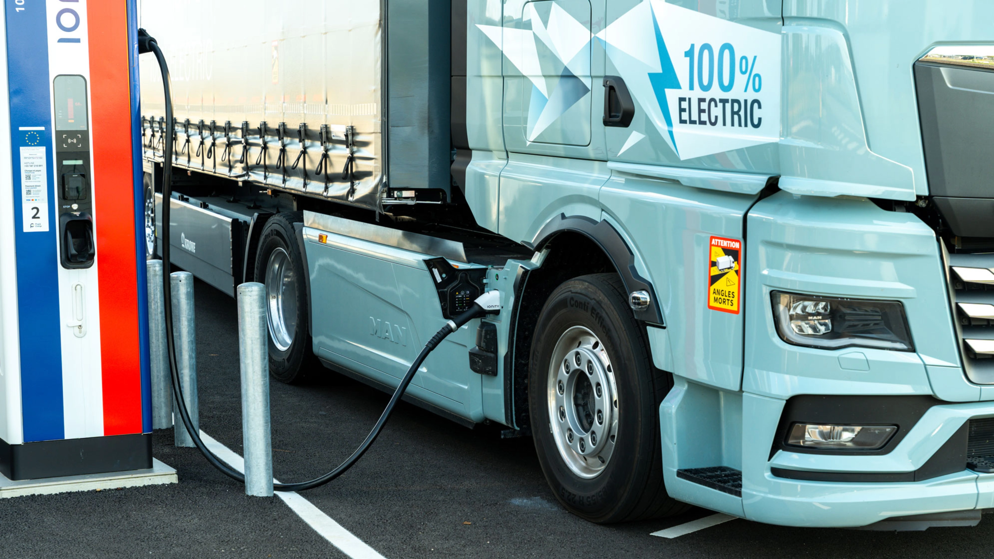 Electric truck charging at a public station, labeled 100% electric.