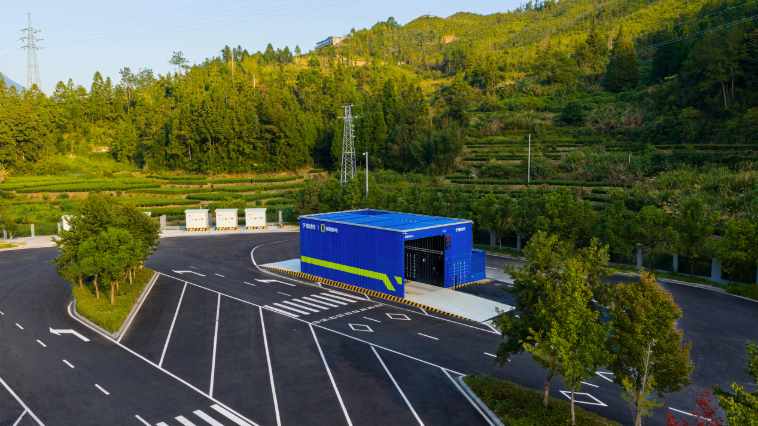 Teststrecke mit Fahrbahnmarkierungen und blauem Gebäude, umgeben von Bäumen und bewaldeten Hügeln.
