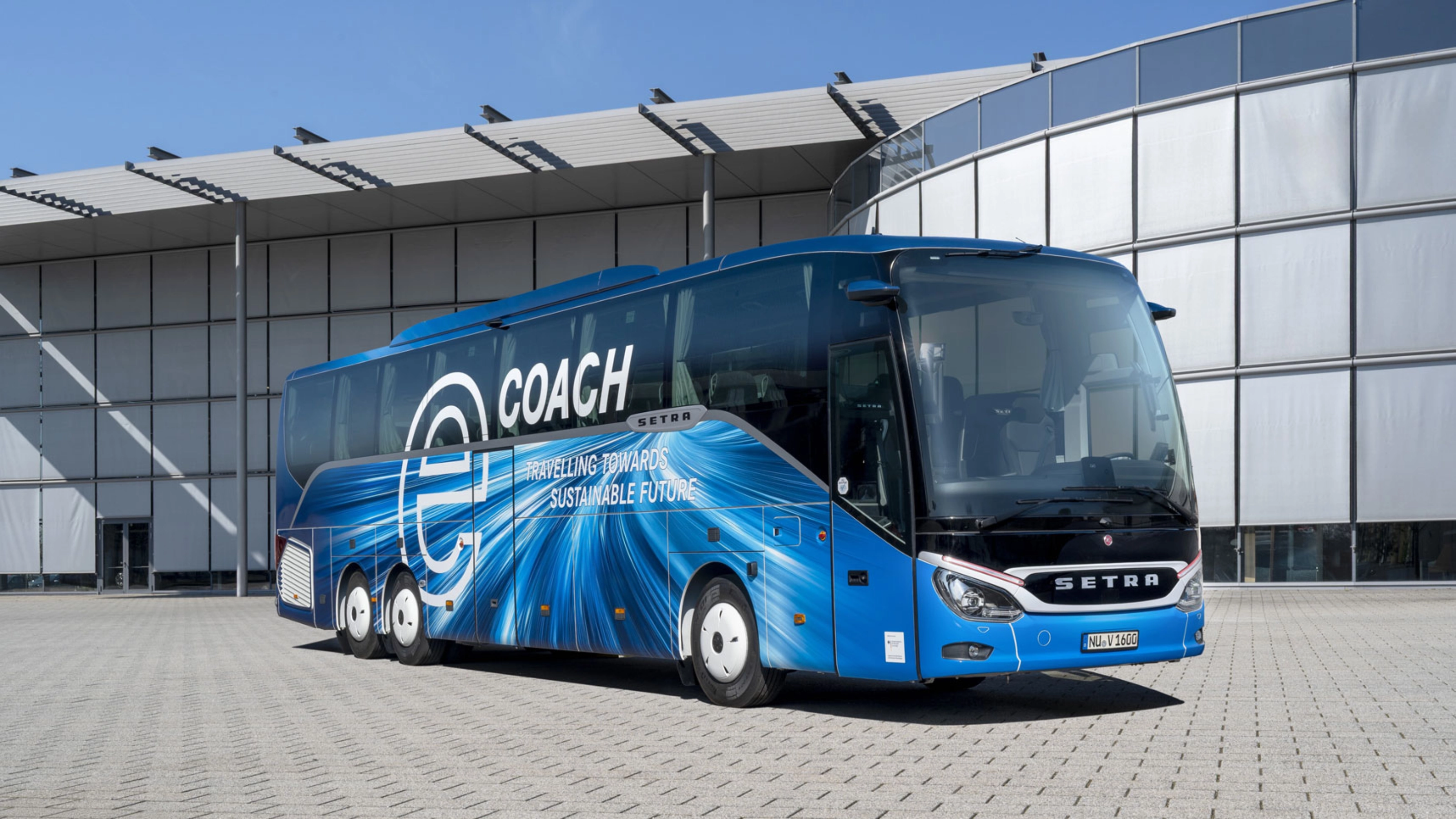 Blauer Setra-Reisebus mit Nachhaltigkeits-Slogan vor modernem Gebäude.