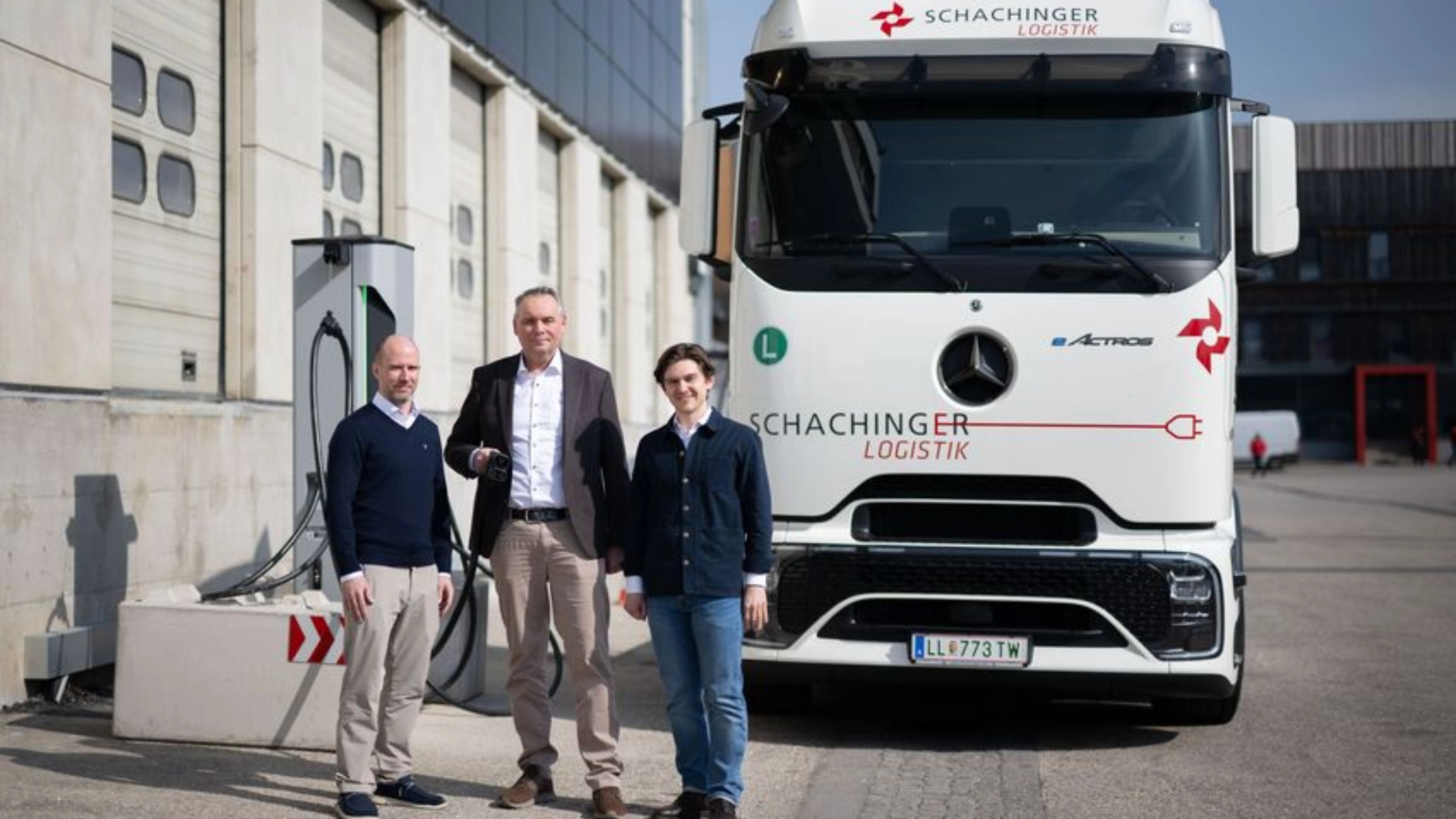 Three men standing in front of a white truck outside an industrial building.