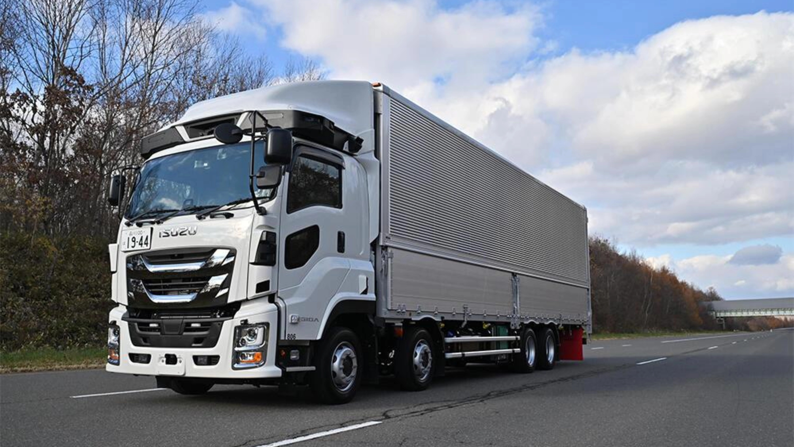White semi-truck with trailer driving on a highway under a cloudy sky.