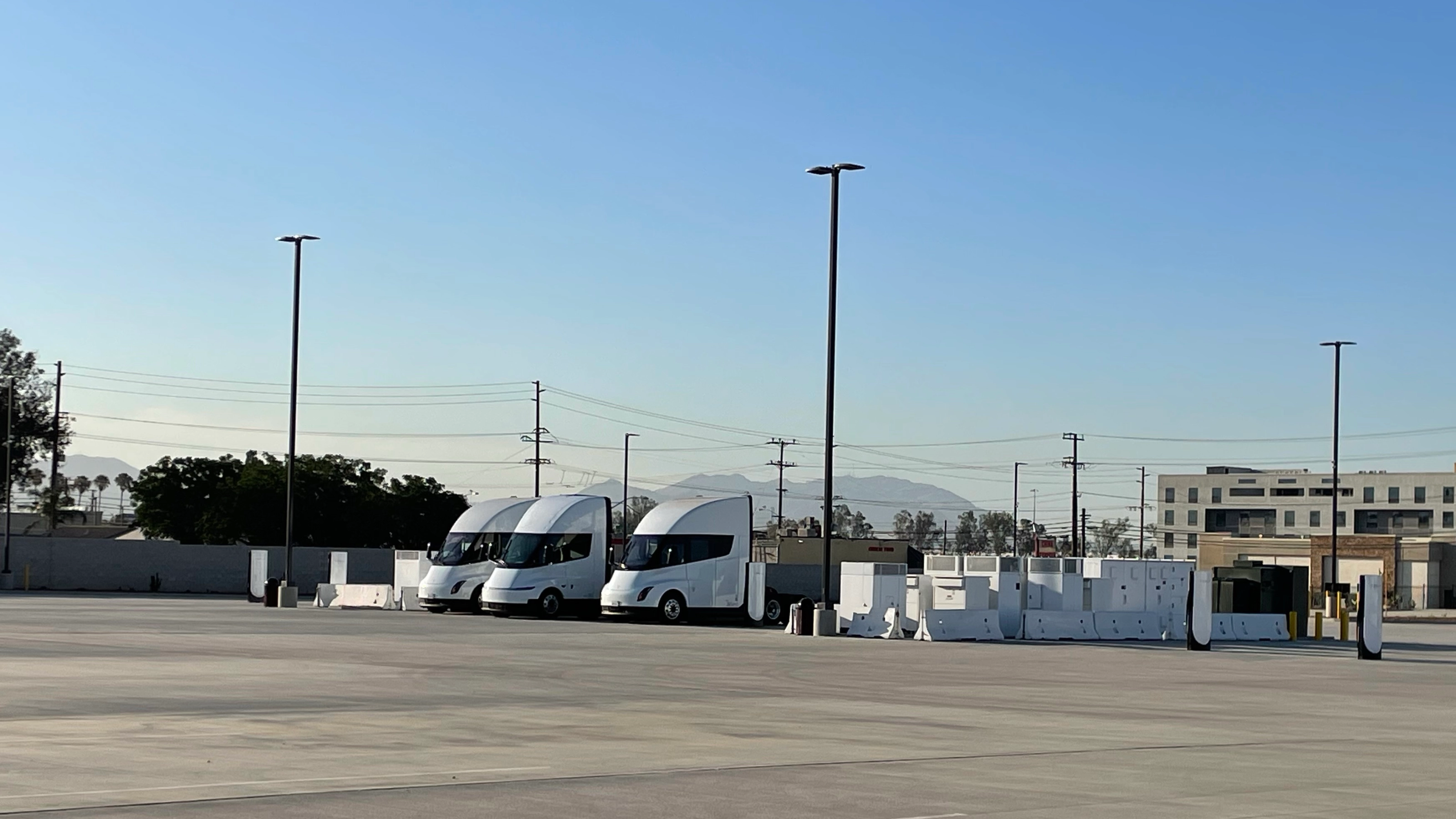 Three white electric trucks are parked at a charging station.