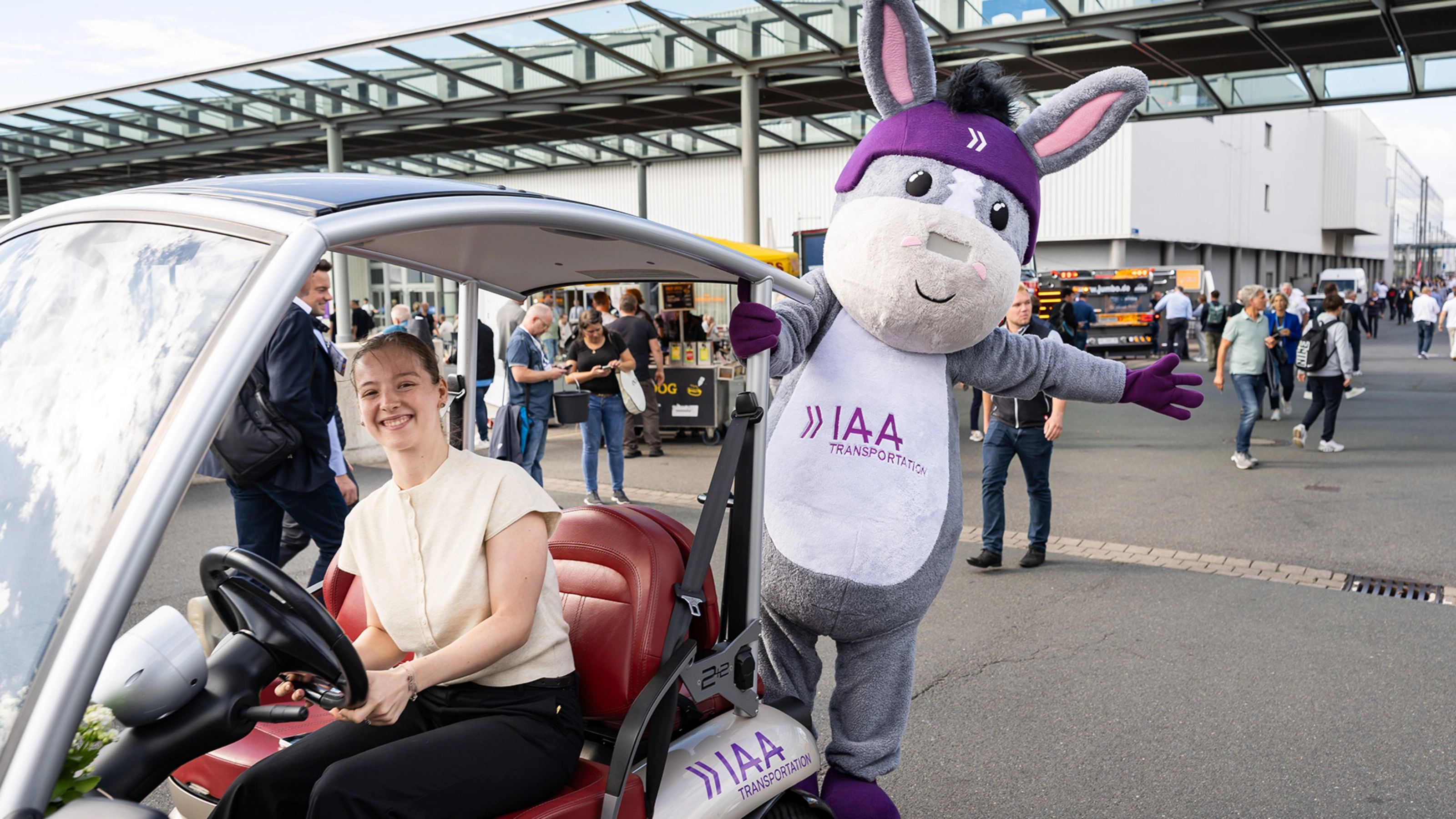 Frau in einem IAA-Fahrzeug neben dem IAA Transportation Maskottchen auf der Messe.