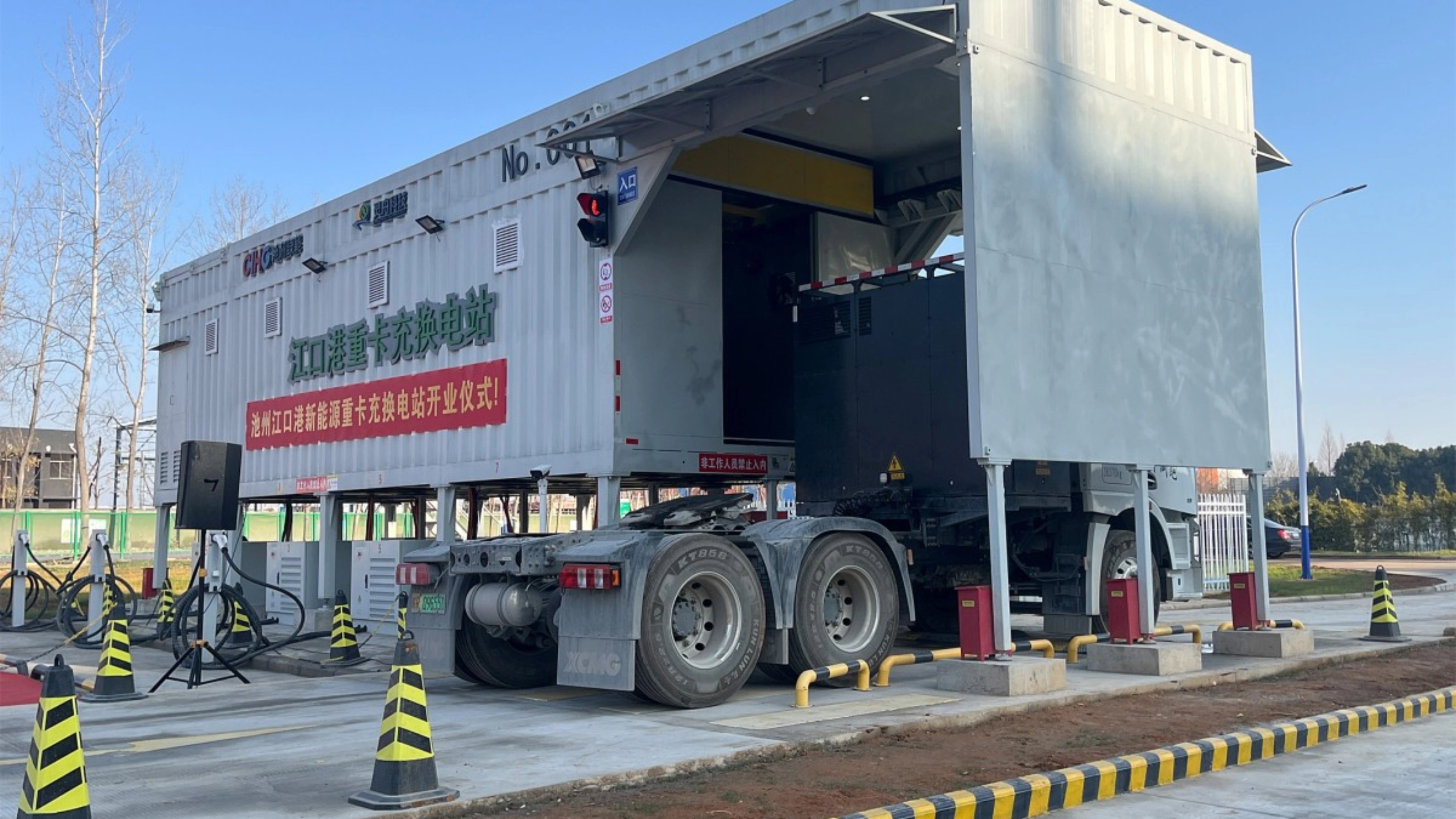 Truck at battery swap station with container module in industrial area.
