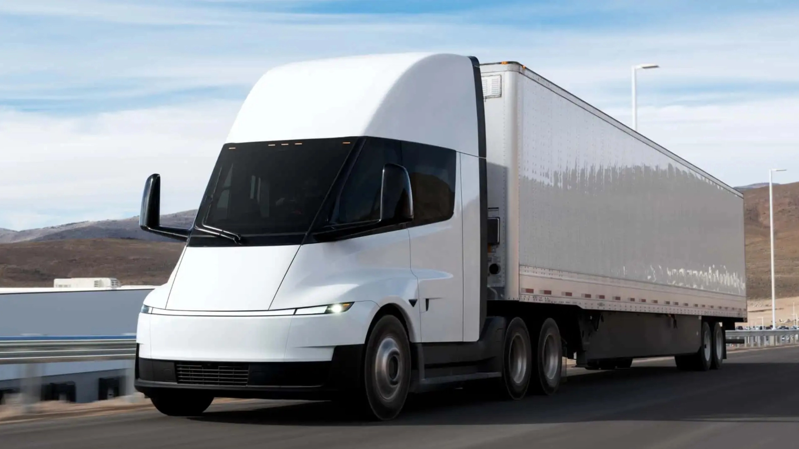 Electric semi-truck driving on a highway in a rural landscape.