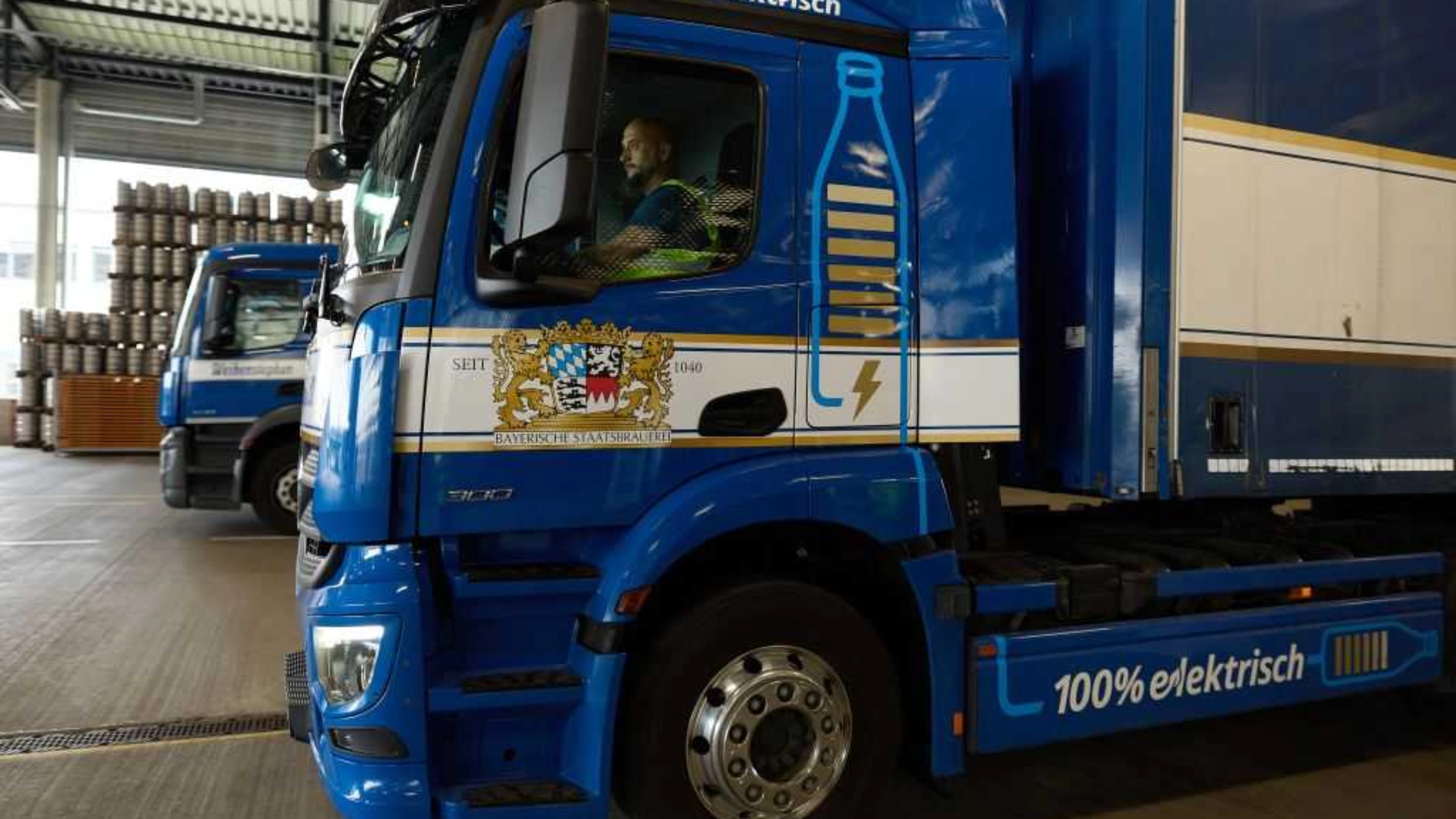 Lastwagen steht in einer Logistikhalle, Fahrer sitzt im Führerhaus.