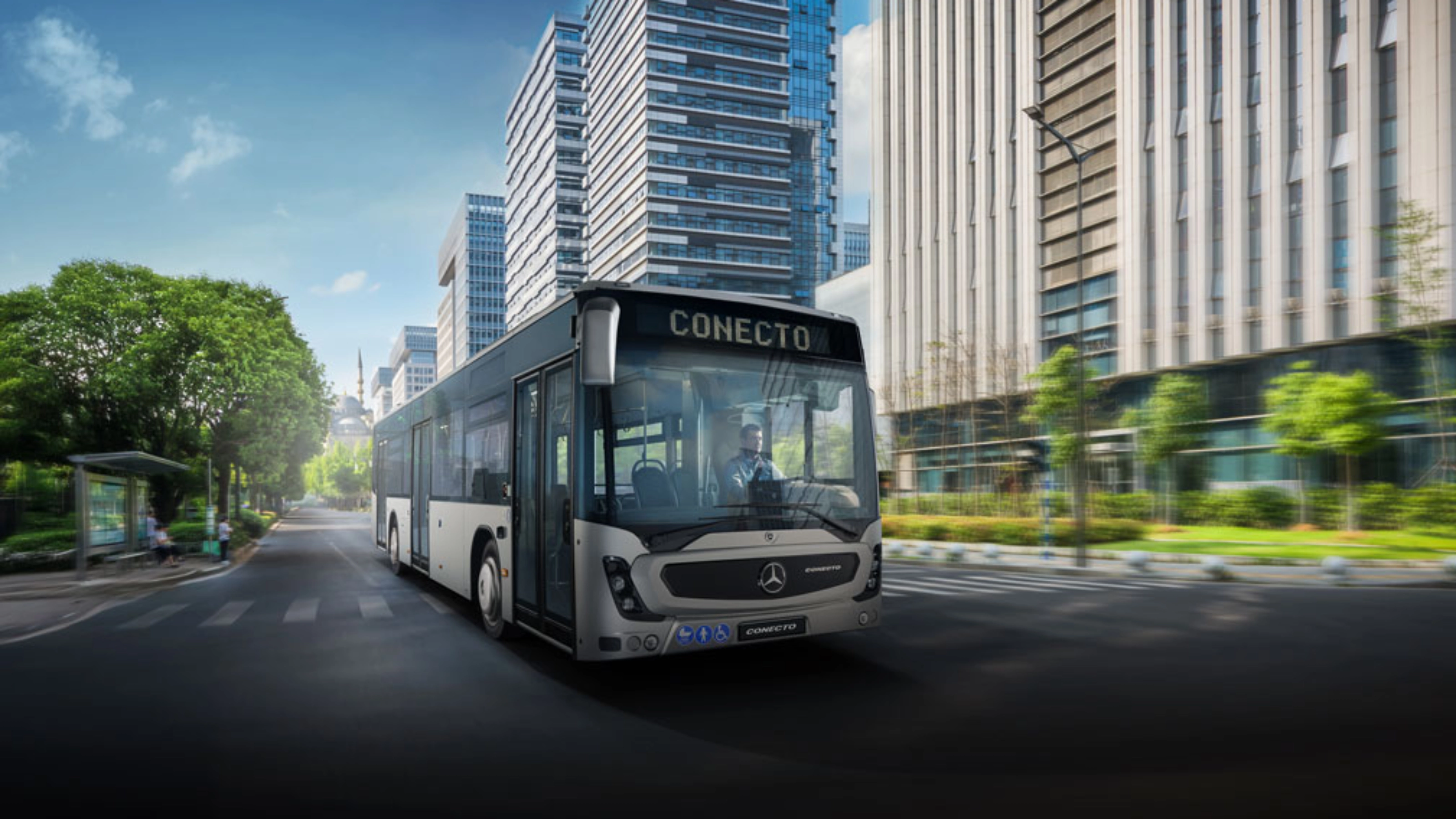 Modern city bus driving on a wide street between tall office buildings.
