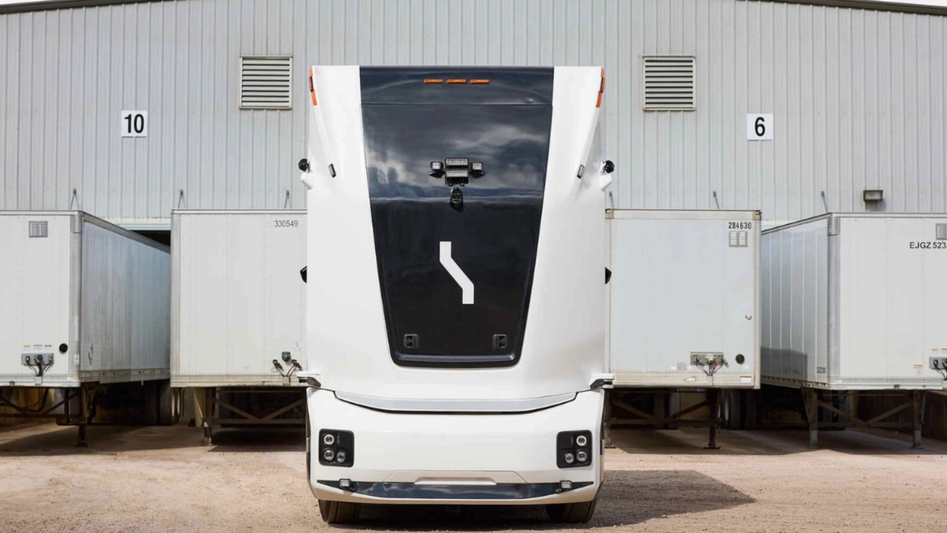 Einride autonomous electric truck in front of a warehouse with trailers.