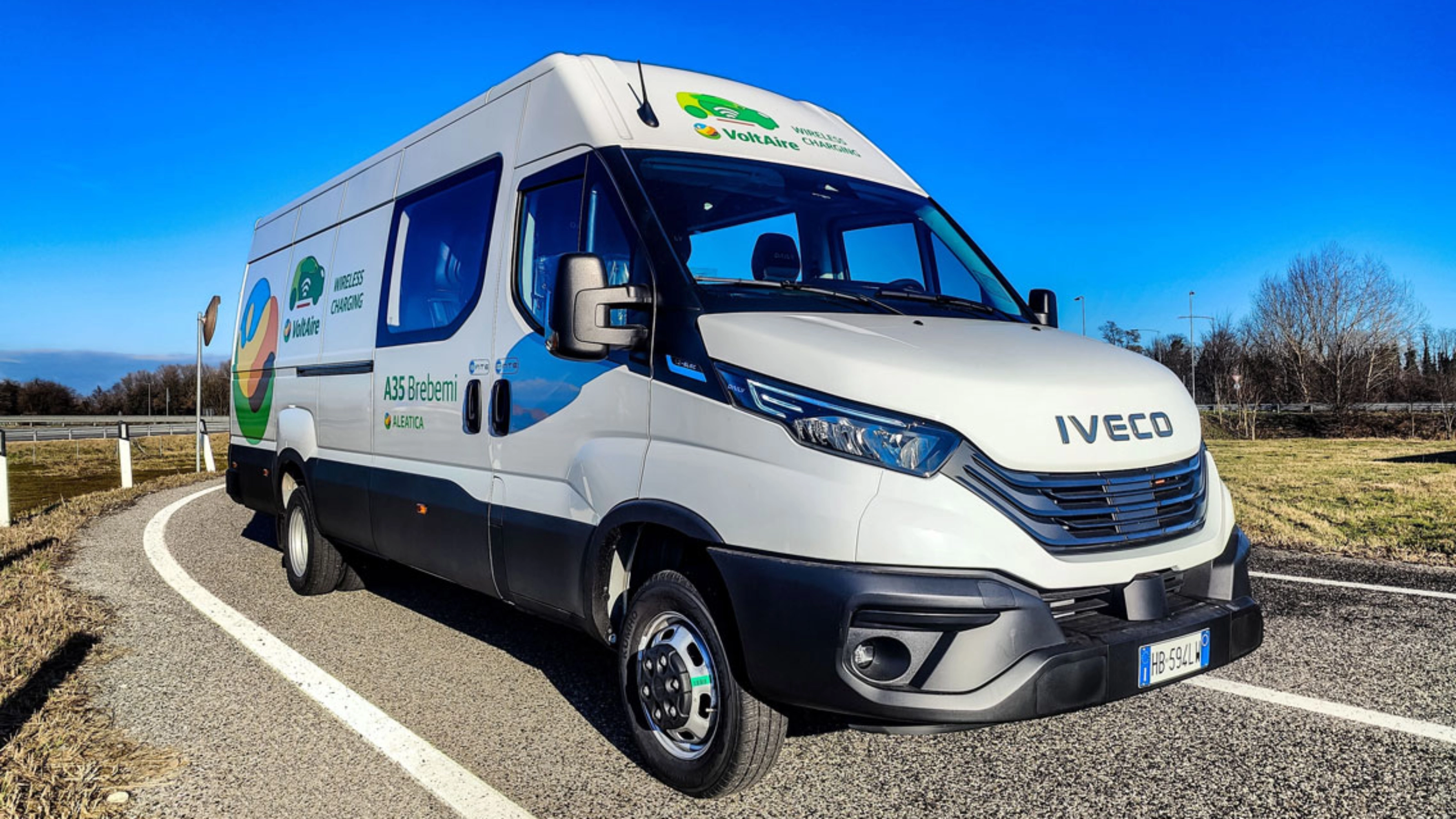 Ein weißer Iveco-Transporter fährt auf einer kurvigen Straße bei blauem Himmel.