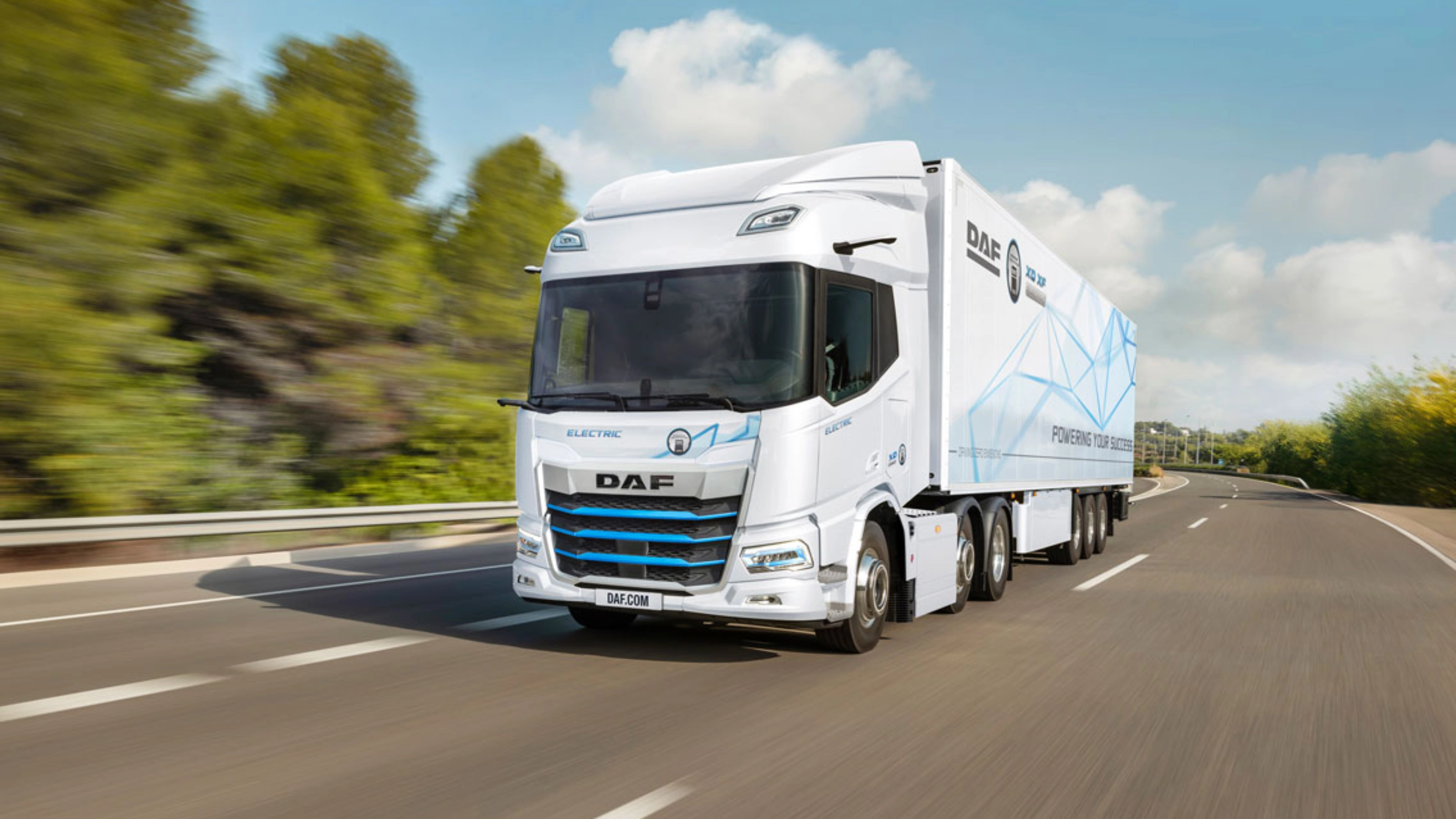 A white DAF electric truck is driving on a curved highway surrounded by greenery.