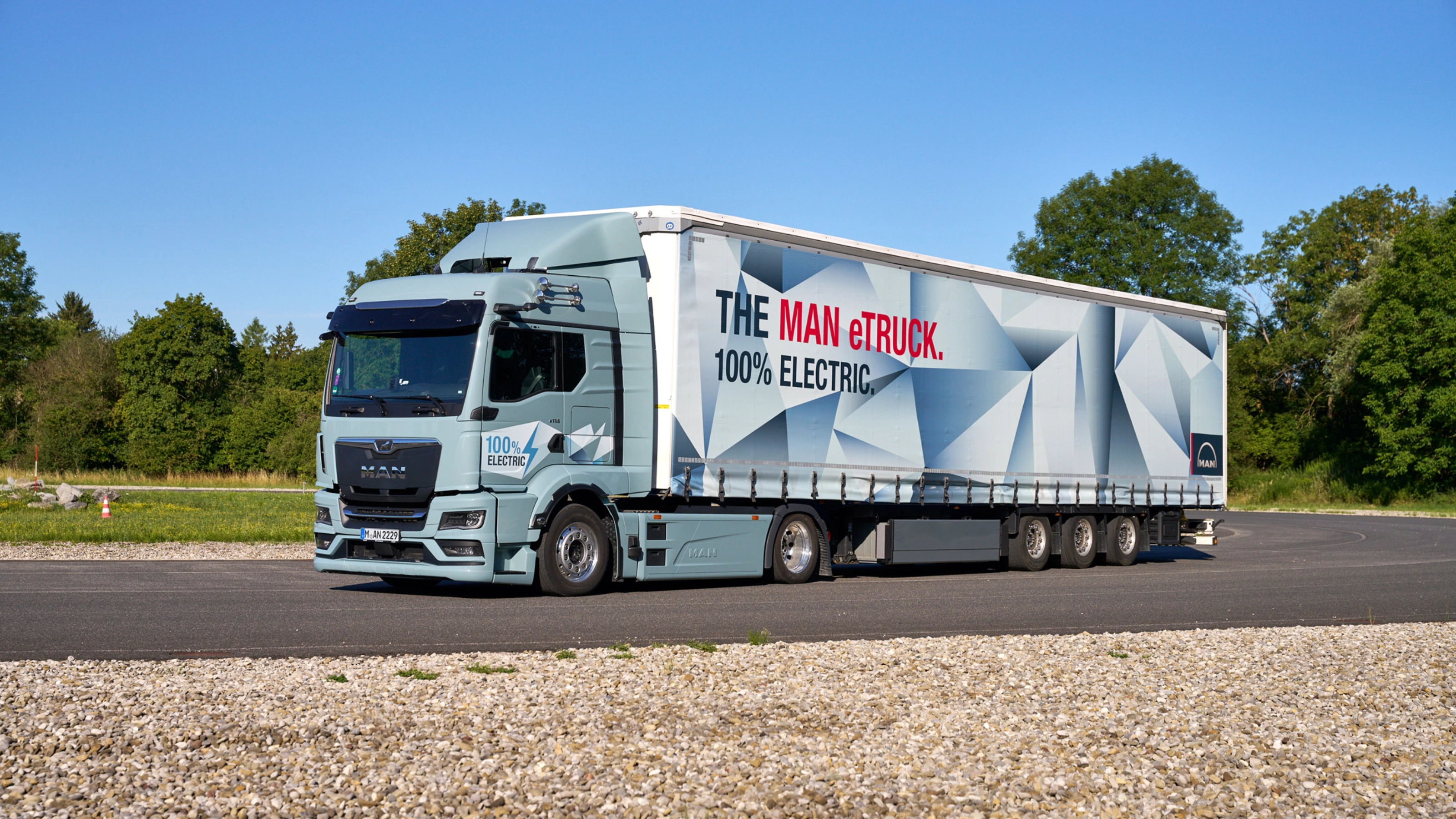 MAN truck with a trailer featuring a large graphic parked on a paved area.
