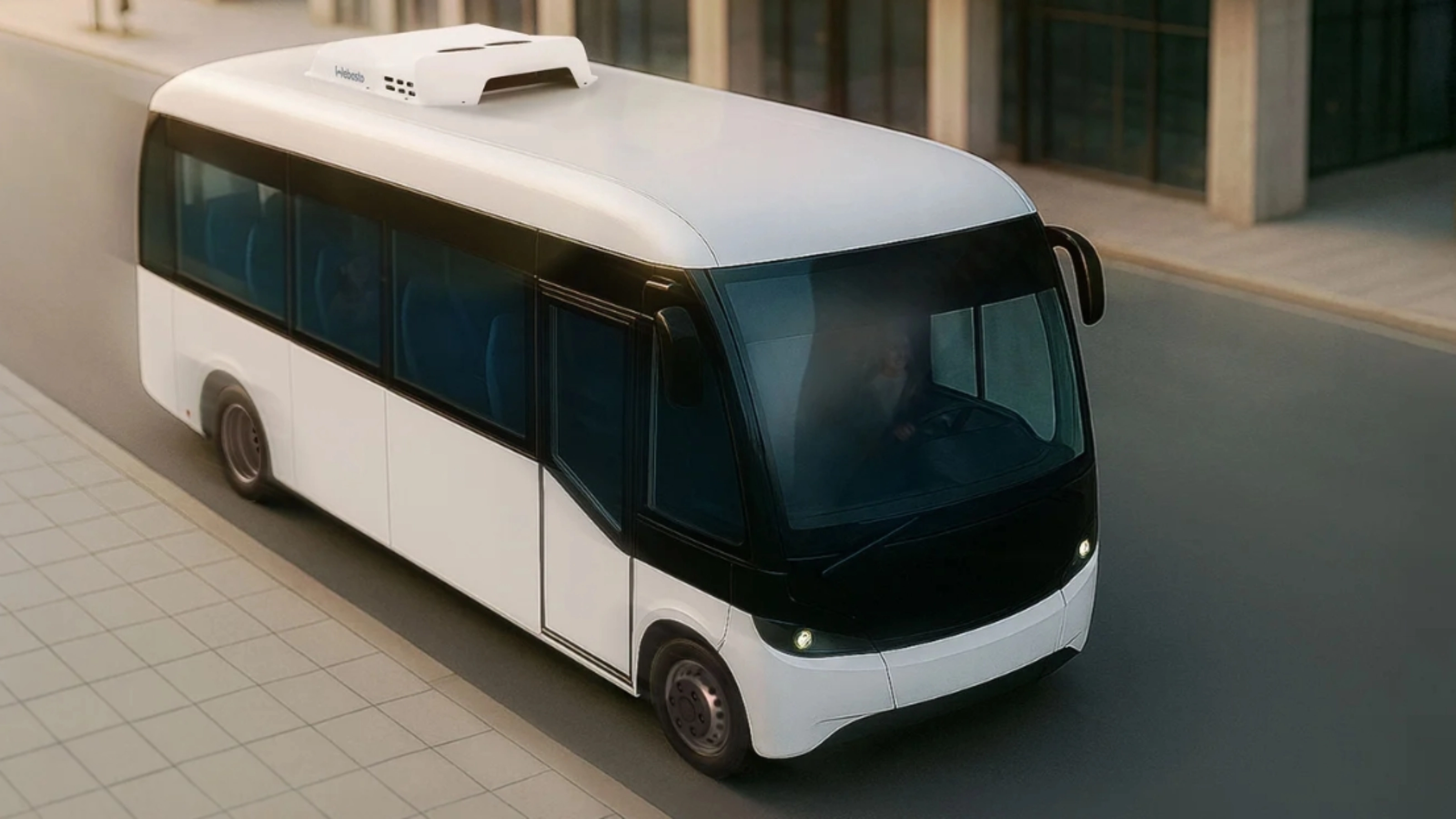 Small white autonomous shuttle bus driving on a city street, viewed from above.