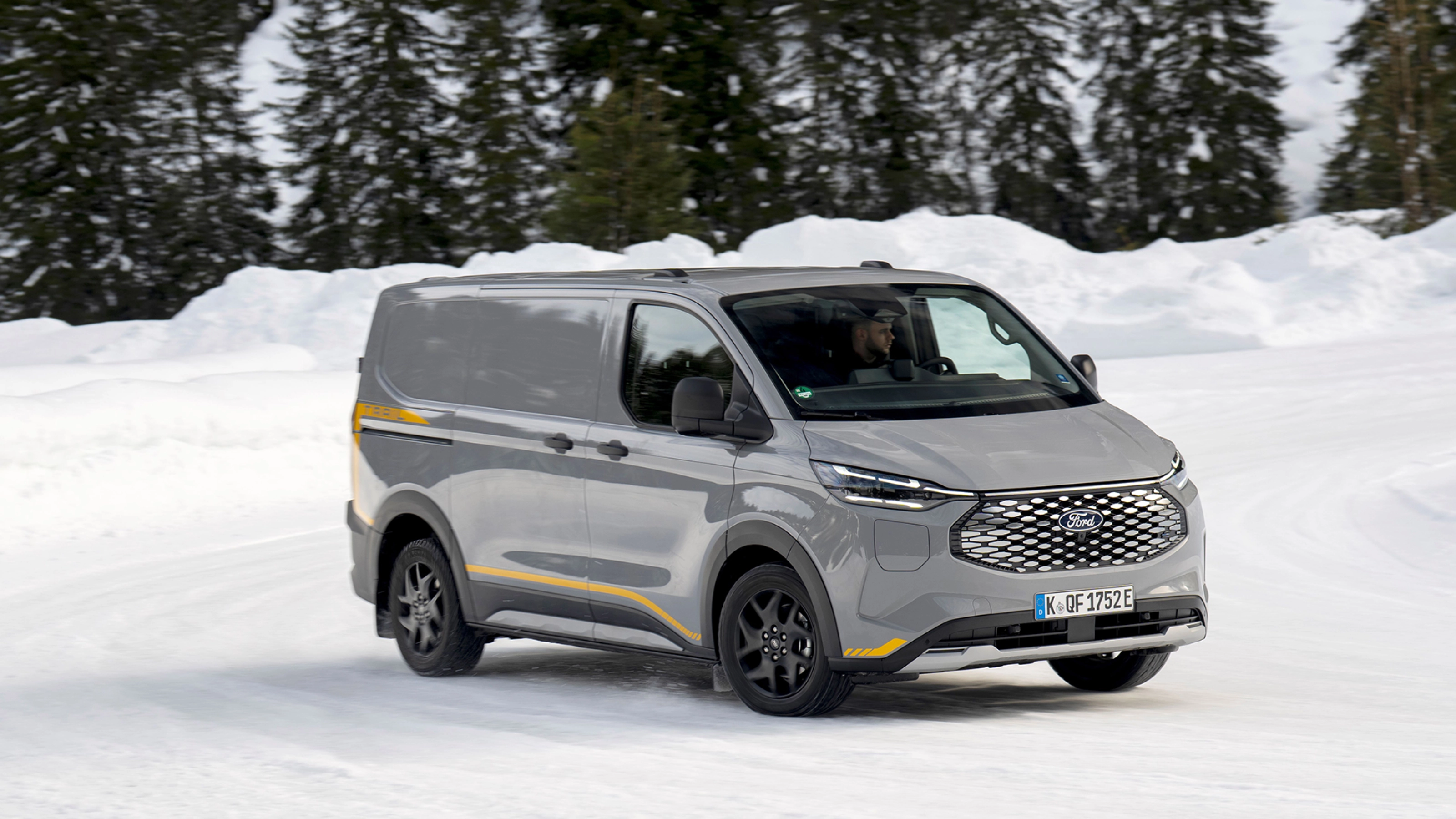 Grey Ford electric van driving on a snowy road with forest in the background.