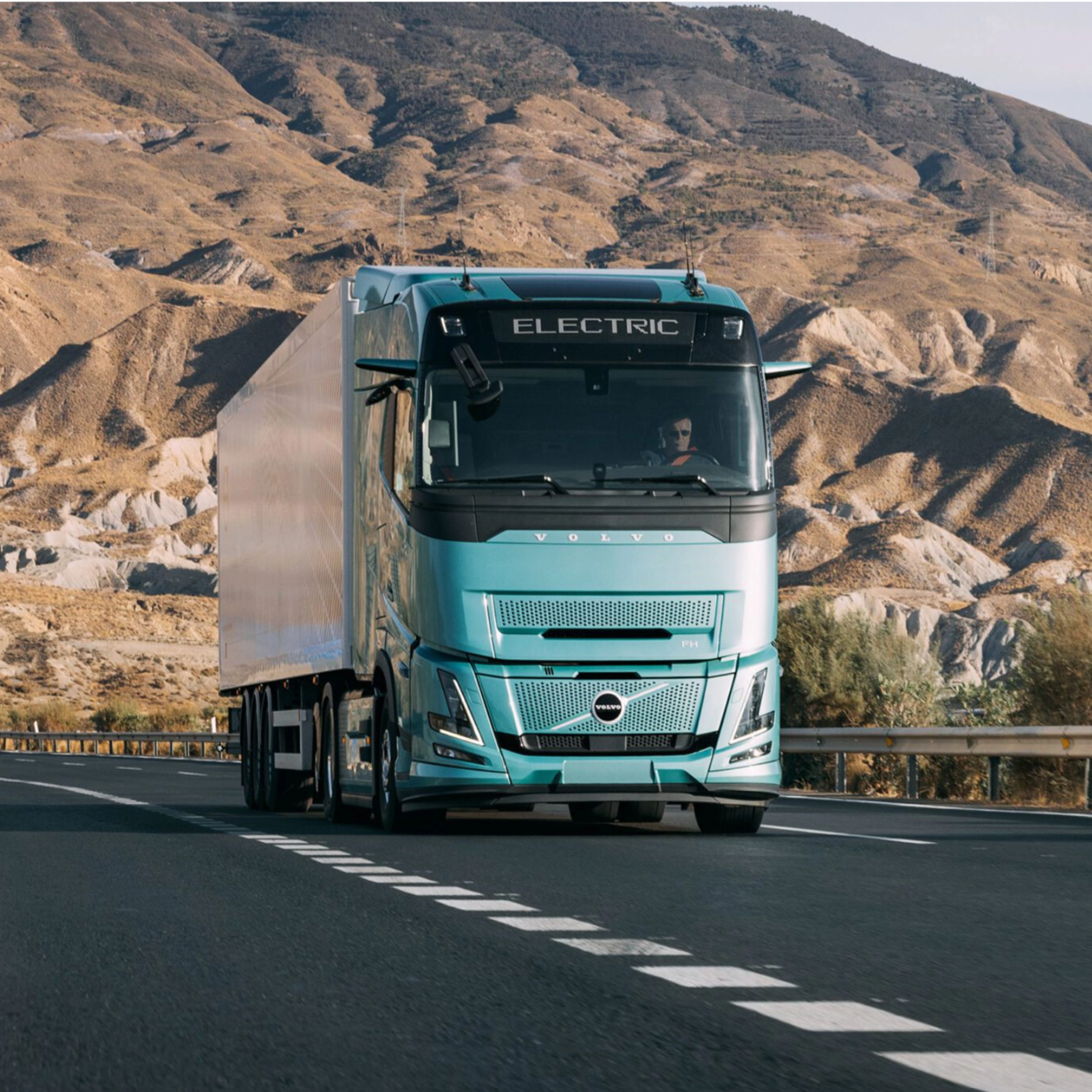 Volvo truck driving on a highway through a rocky desert landscape.