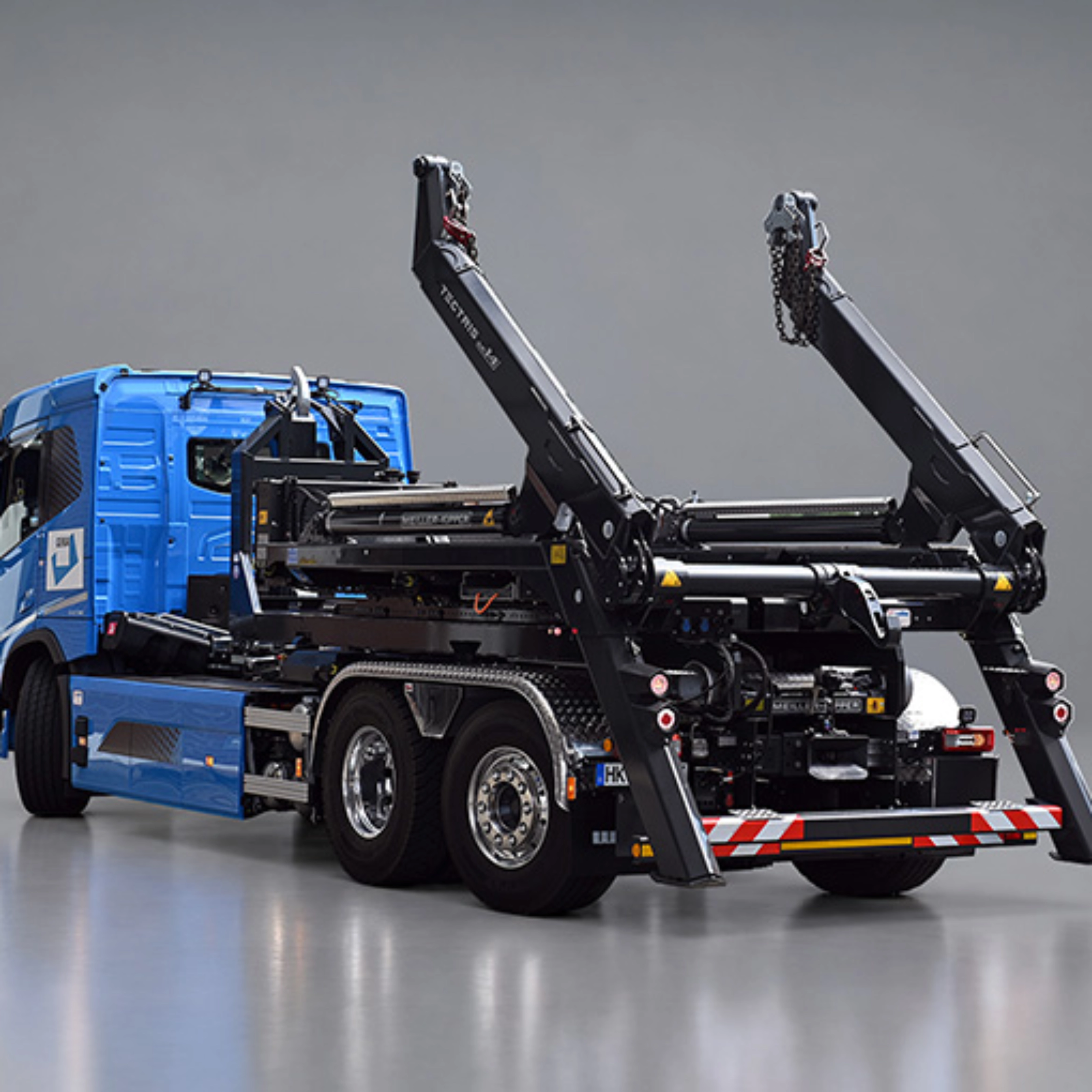 Blauer Lkw mit schwarzem Meiller-Hakenliftsystem und angehobenen Hubarmen in schräger Rückansicht.