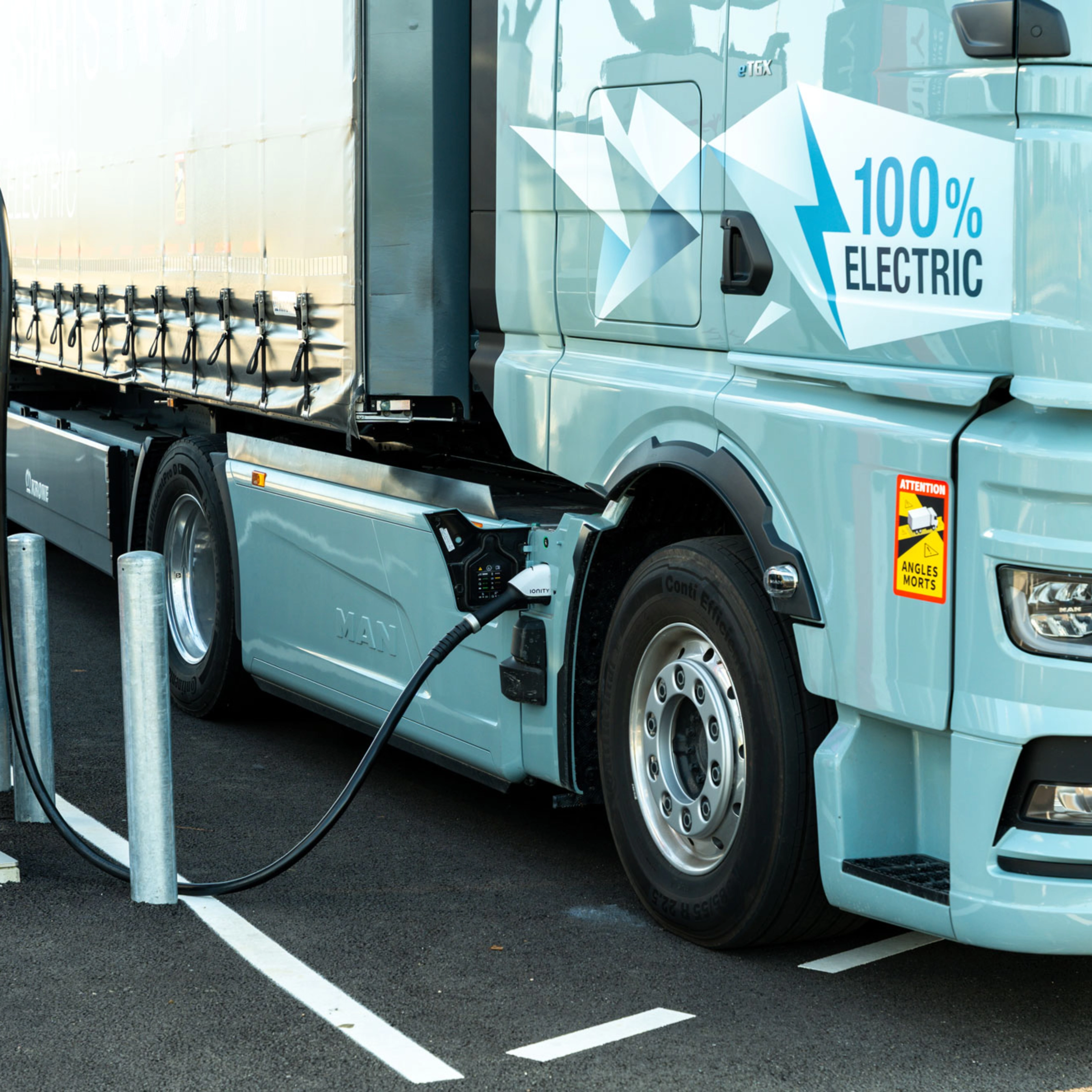 Electric truck charging at a public station, labeled 100% electric.