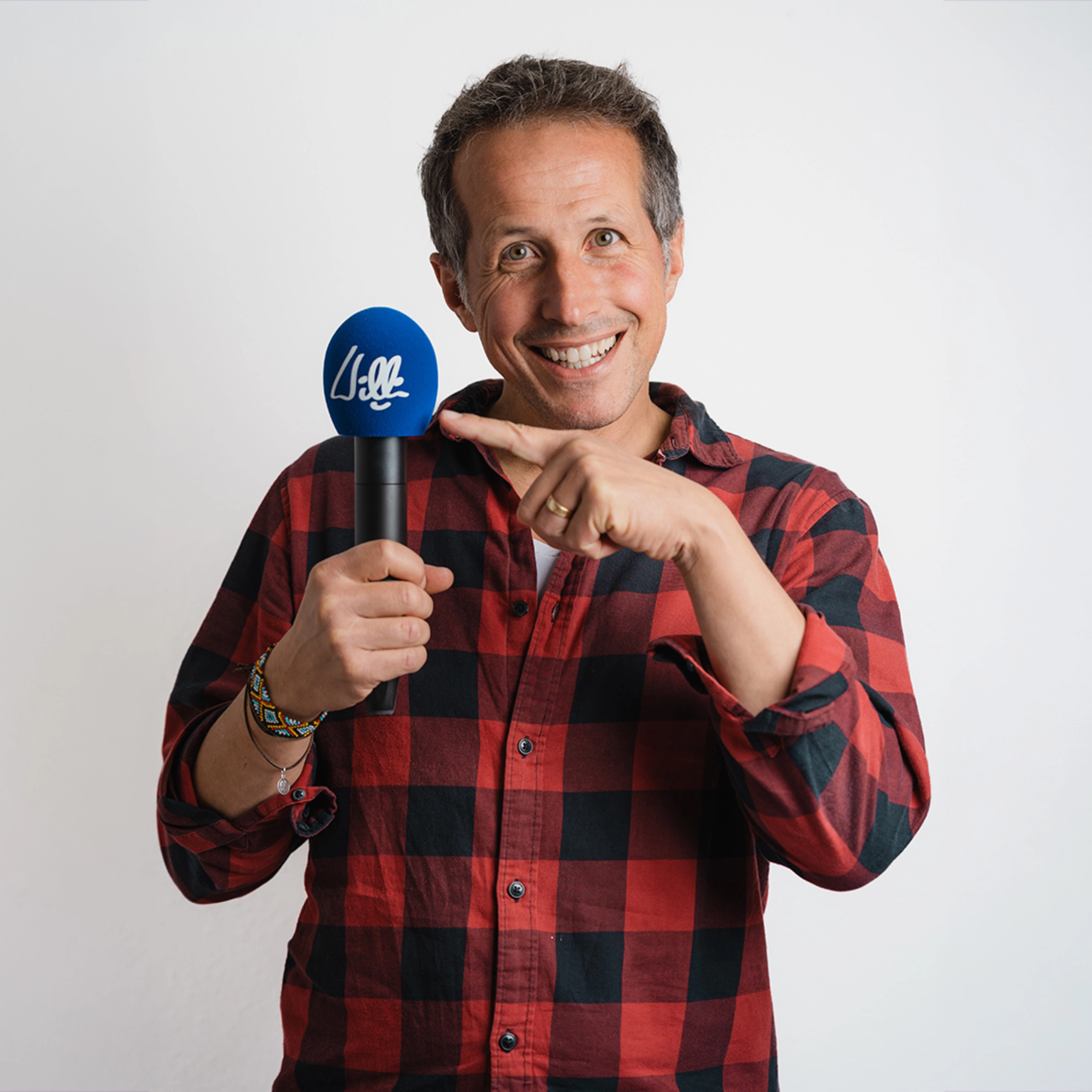 Willi Weitzel lächelt und zeigt in einem Porträt auf ein Mikrofon.