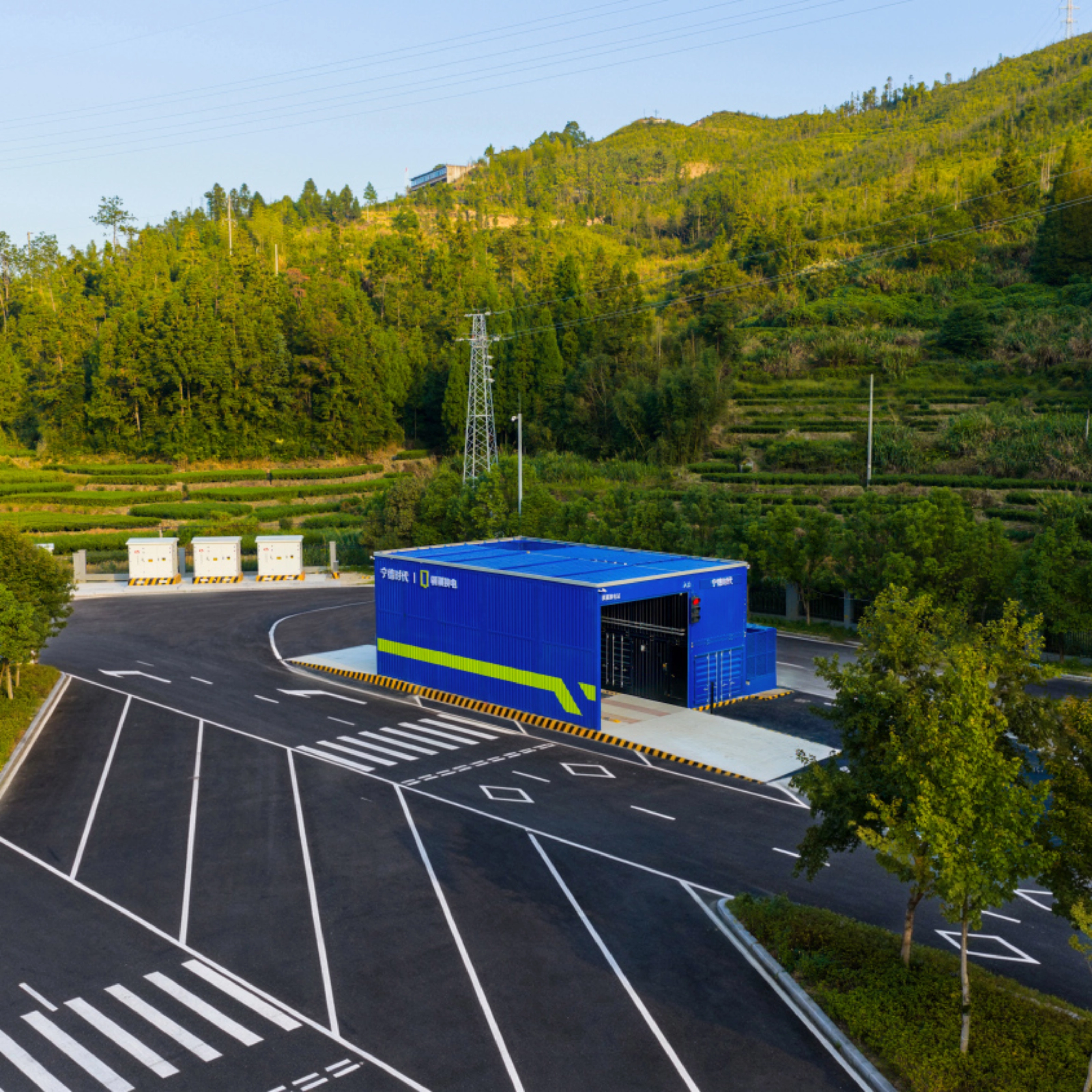 Teststrecke mit Fahrbahnmarkierungen und blauem Gebäude, umgeben von Bäumen und bewaldeten Hügeln.