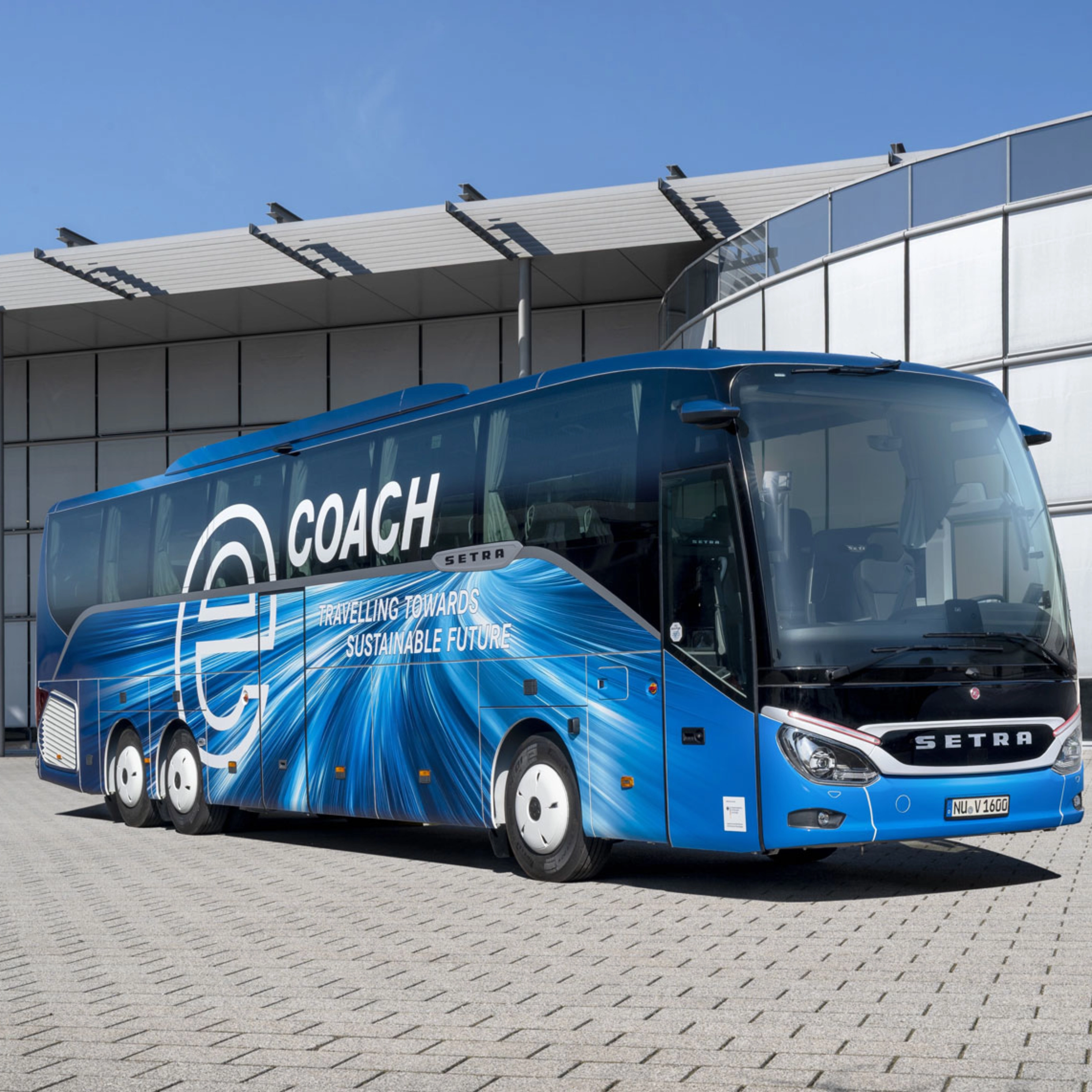 Blauer Setra-Reisebus mit Nachhaltigkeits-Slogan vor modernem Gebäude.