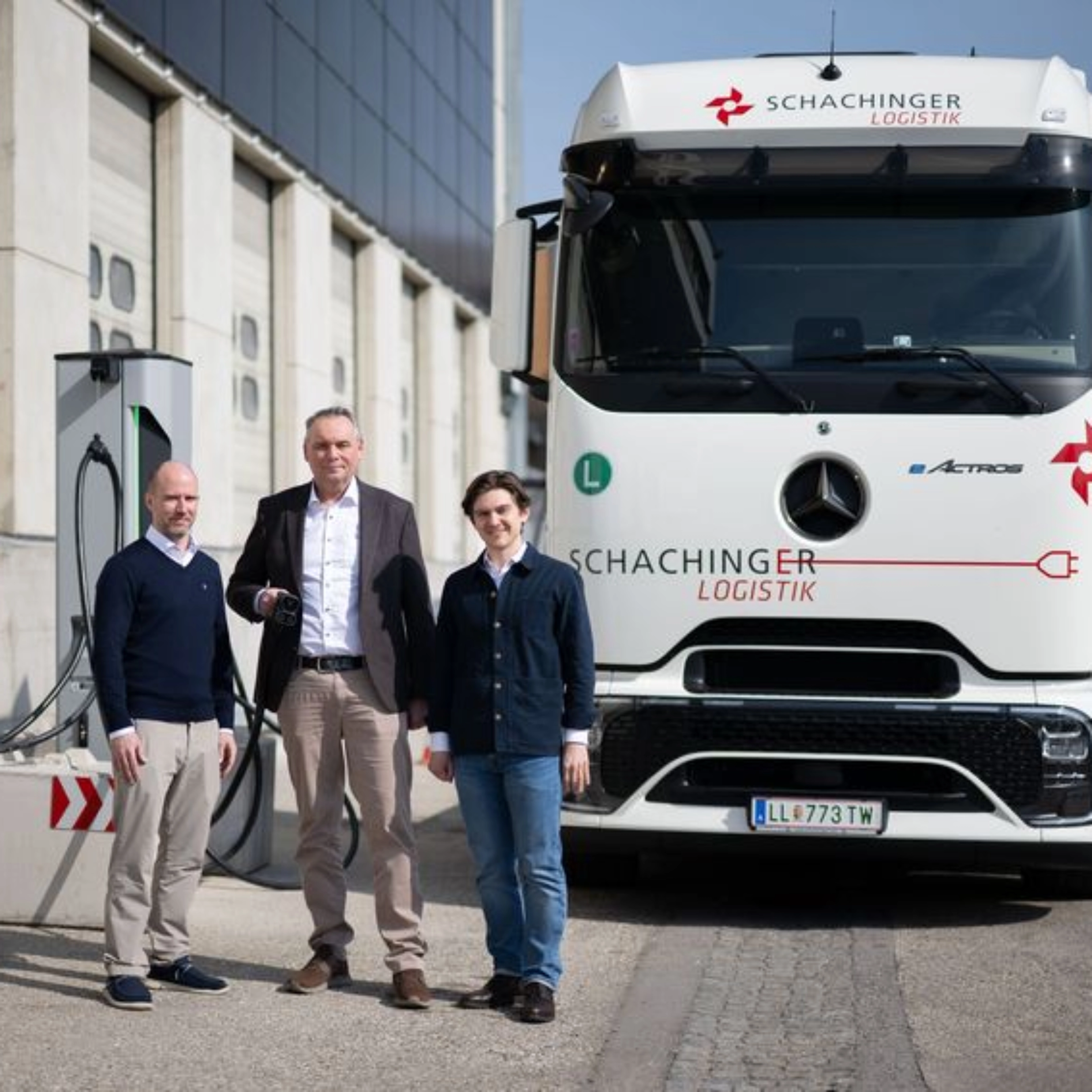 Three men standing in front of a white truck outside an industrial building.