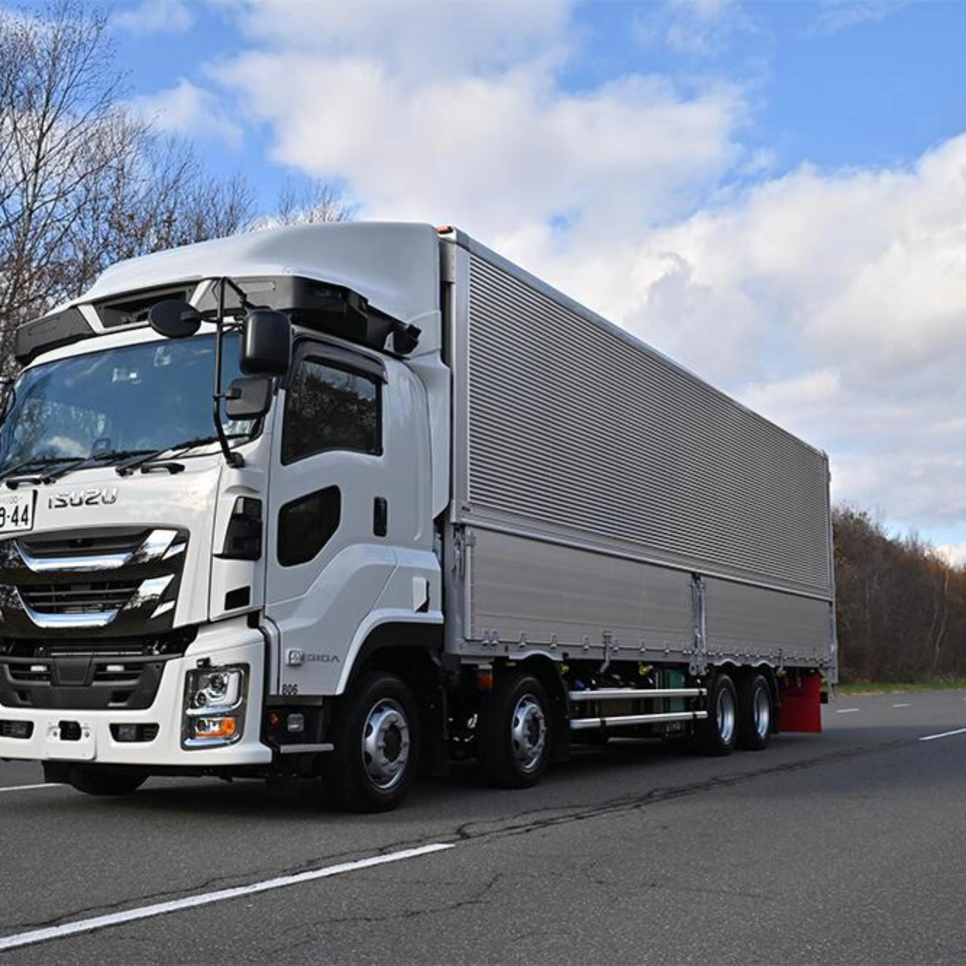 White semi-truck with trailer driving on a highway under a cloudy sky.