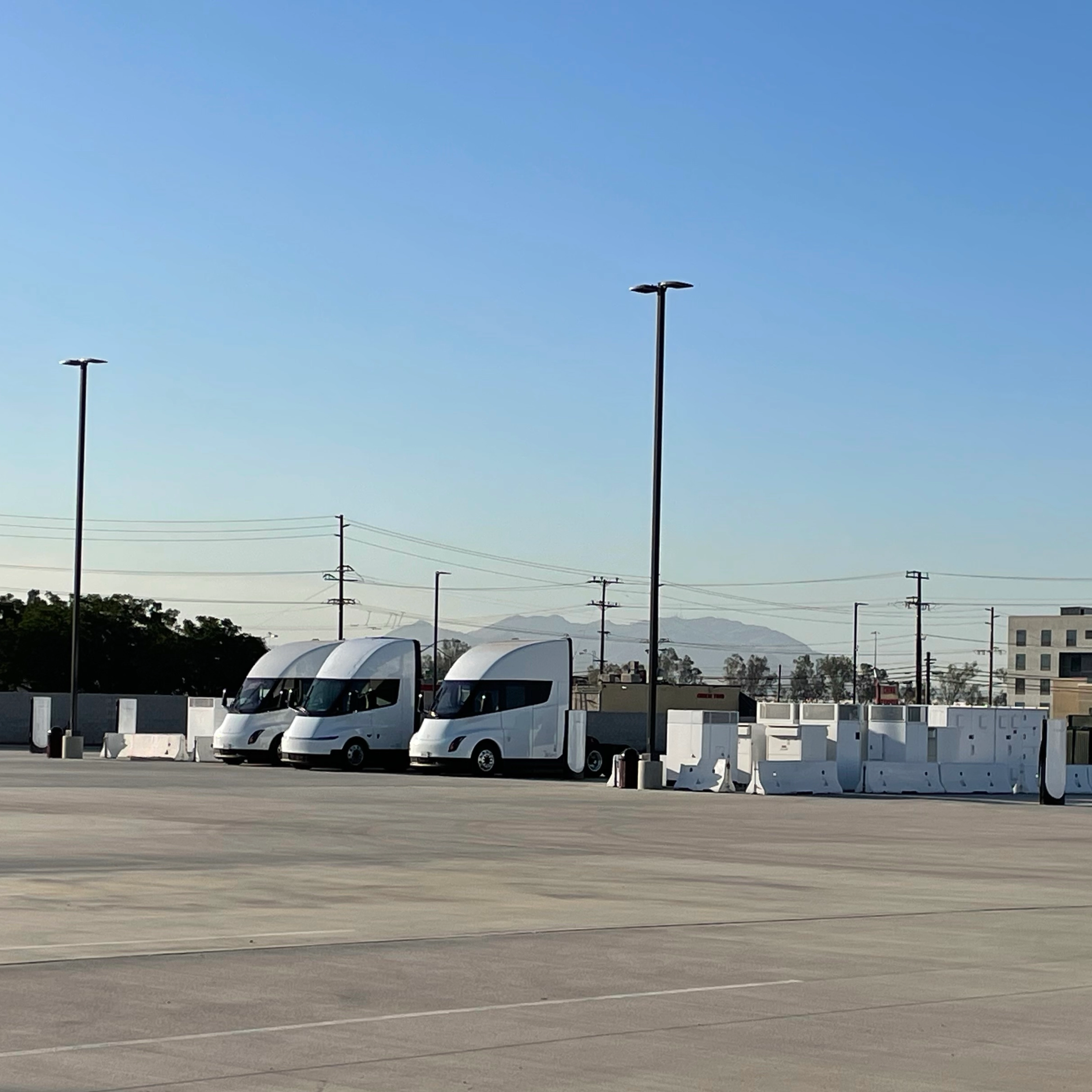 Three white electric trucks are parked at a charging station.