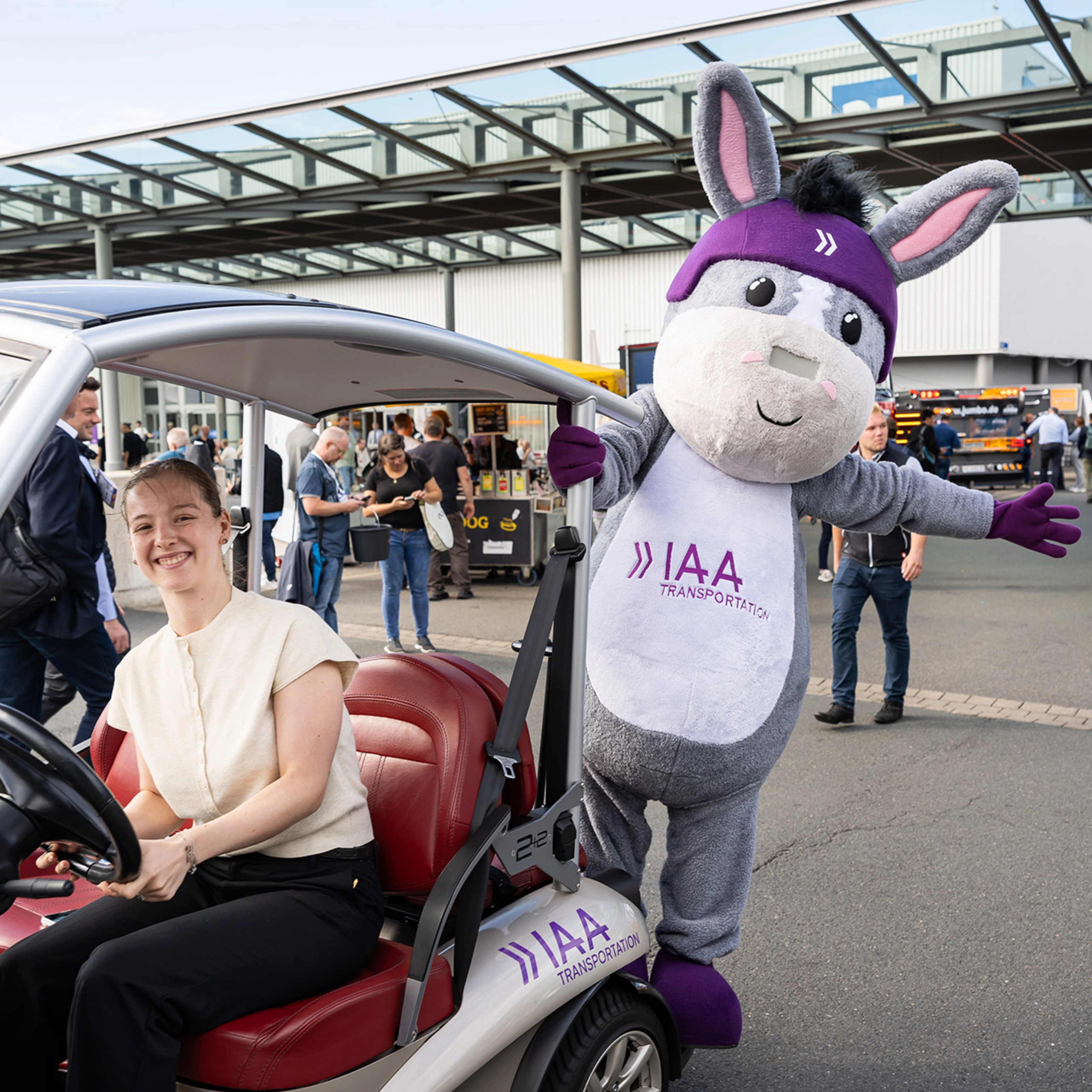 Frau in einem IAA-Fahrzeug neben dem IAA Transportation Maskottchen auf der Messe.