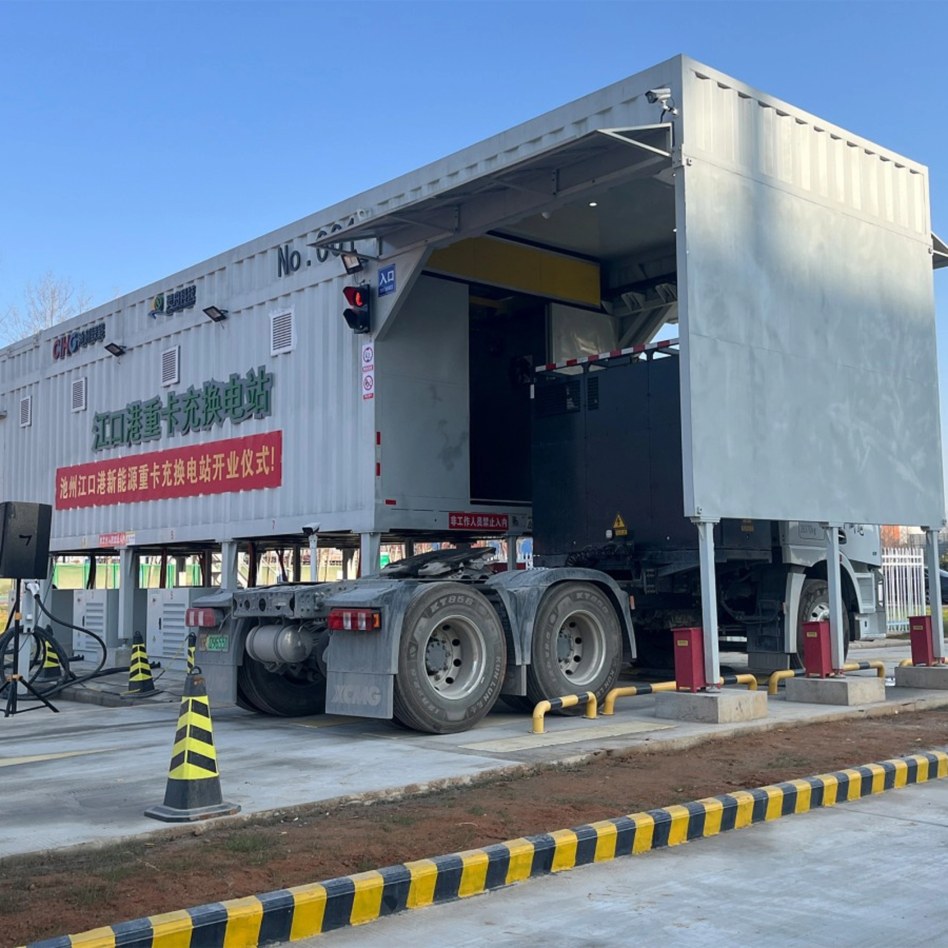 Truck at battery swap station with container module in industrial area.