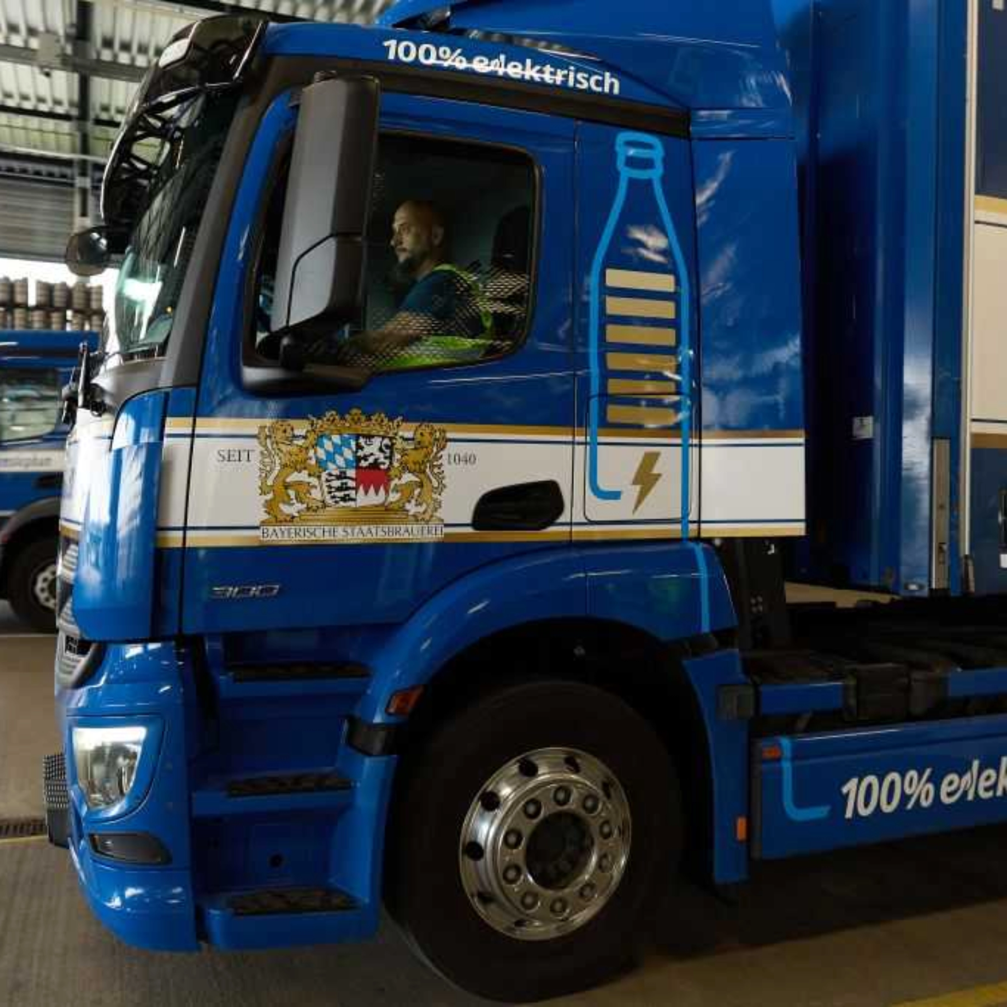 Lastwagen steht in einer Logistikhalle, Fahrer sitzt im Führerhaus.