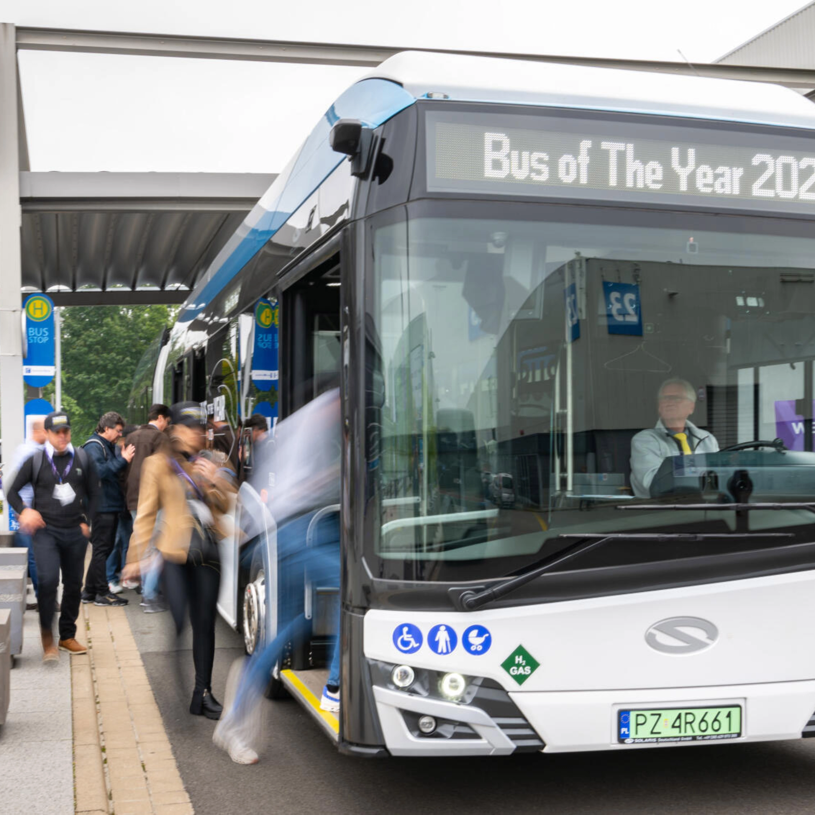 Hydrogen shuttle bus marked “Bus of The Year 2025” at a busy bus stop.