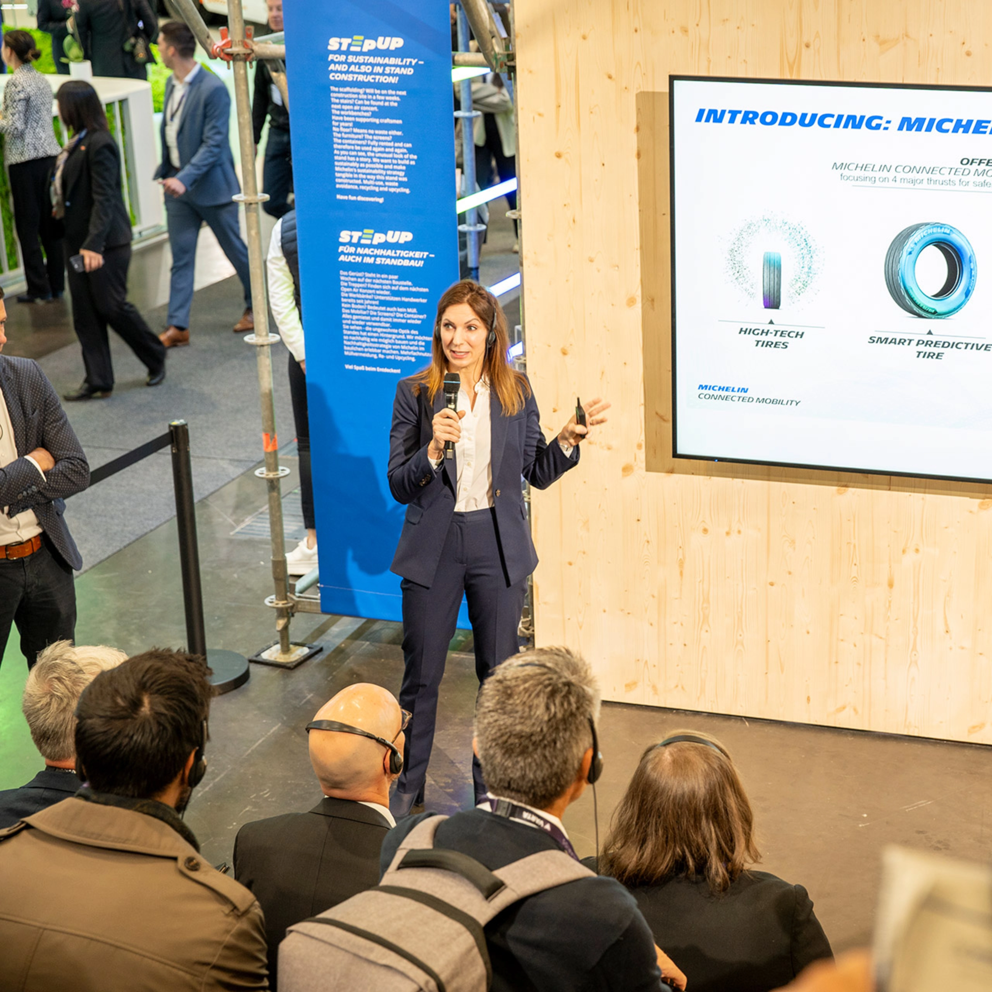 Woman presents Michelin Connected Mobility to audience at trade fair booth.