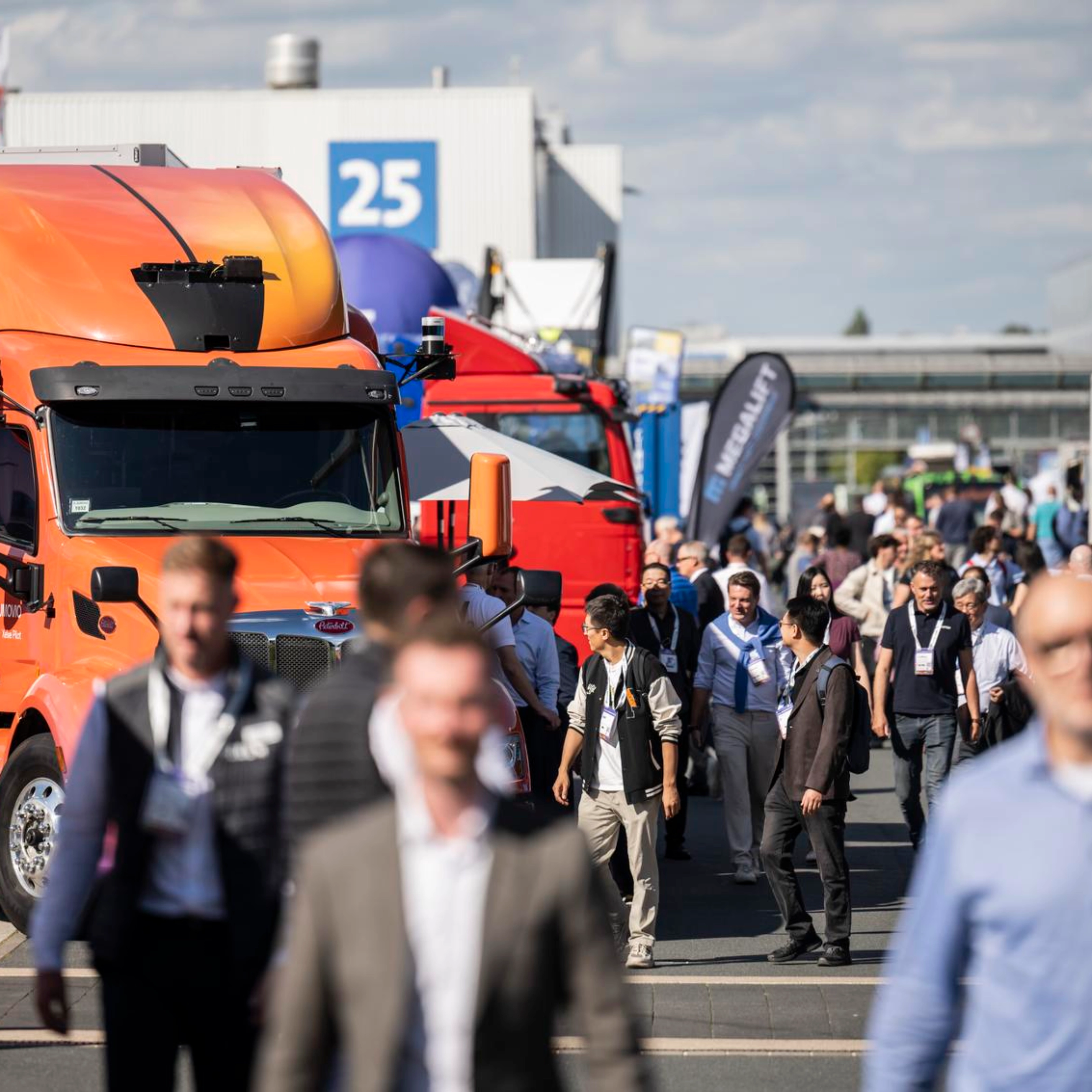Besucher gehen auf einem belebten Messegelände zwischen Lkw hindurch.