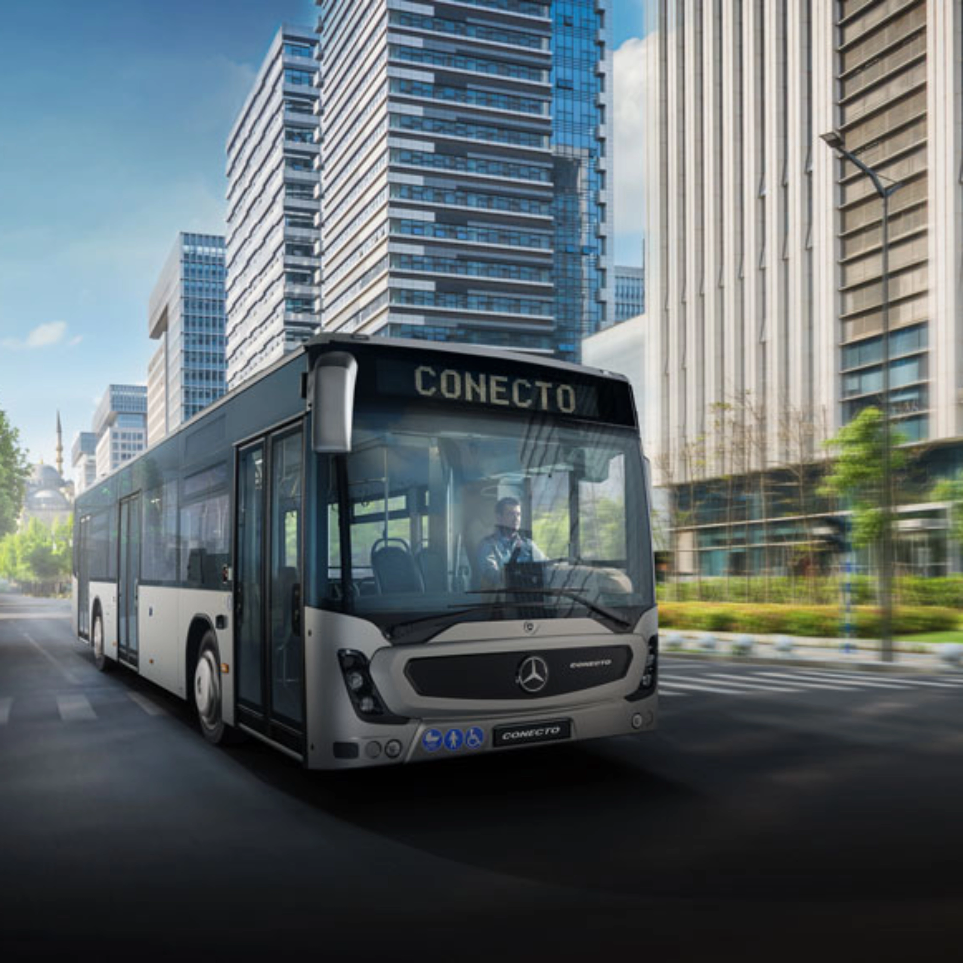 Modern city bus driving on a wide street between tall office buildings.