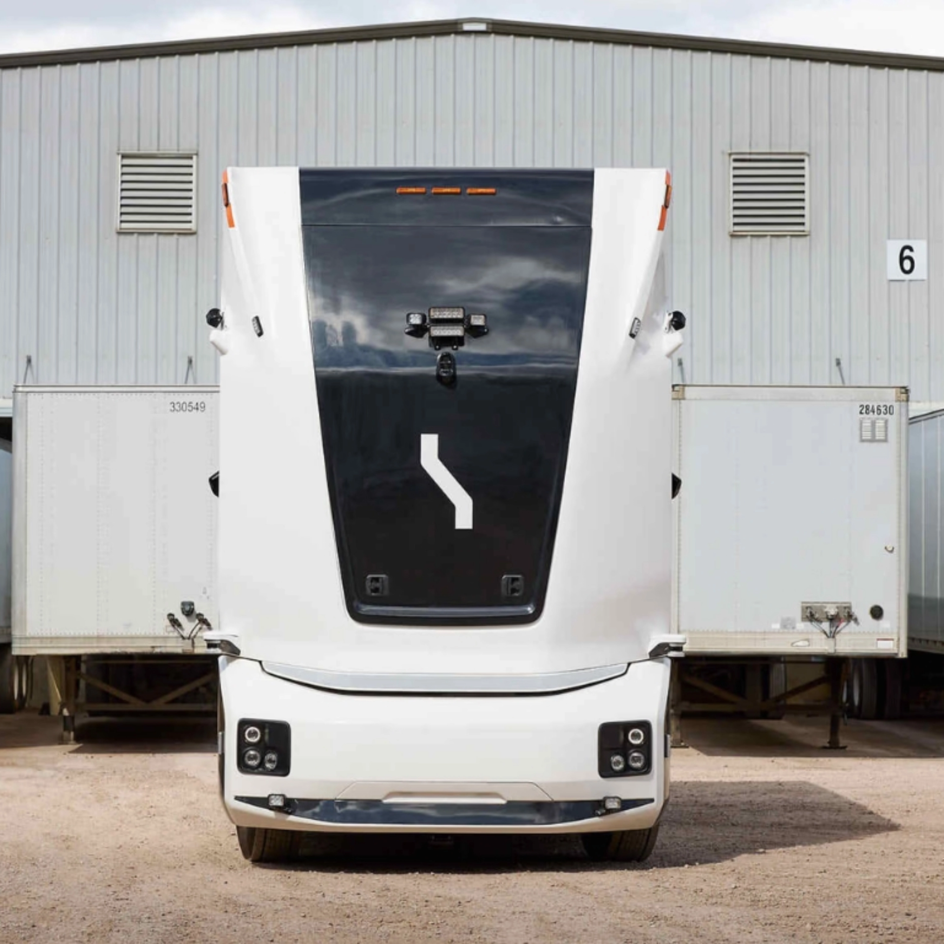 Einride autonomous electric truck in front of a warehouse with trailers.